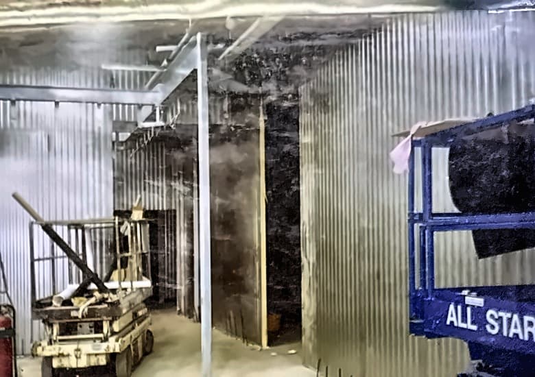 Interior of a cold room under construction, metal-clad walls, a ride-on floor machine and a rolling scaffold.