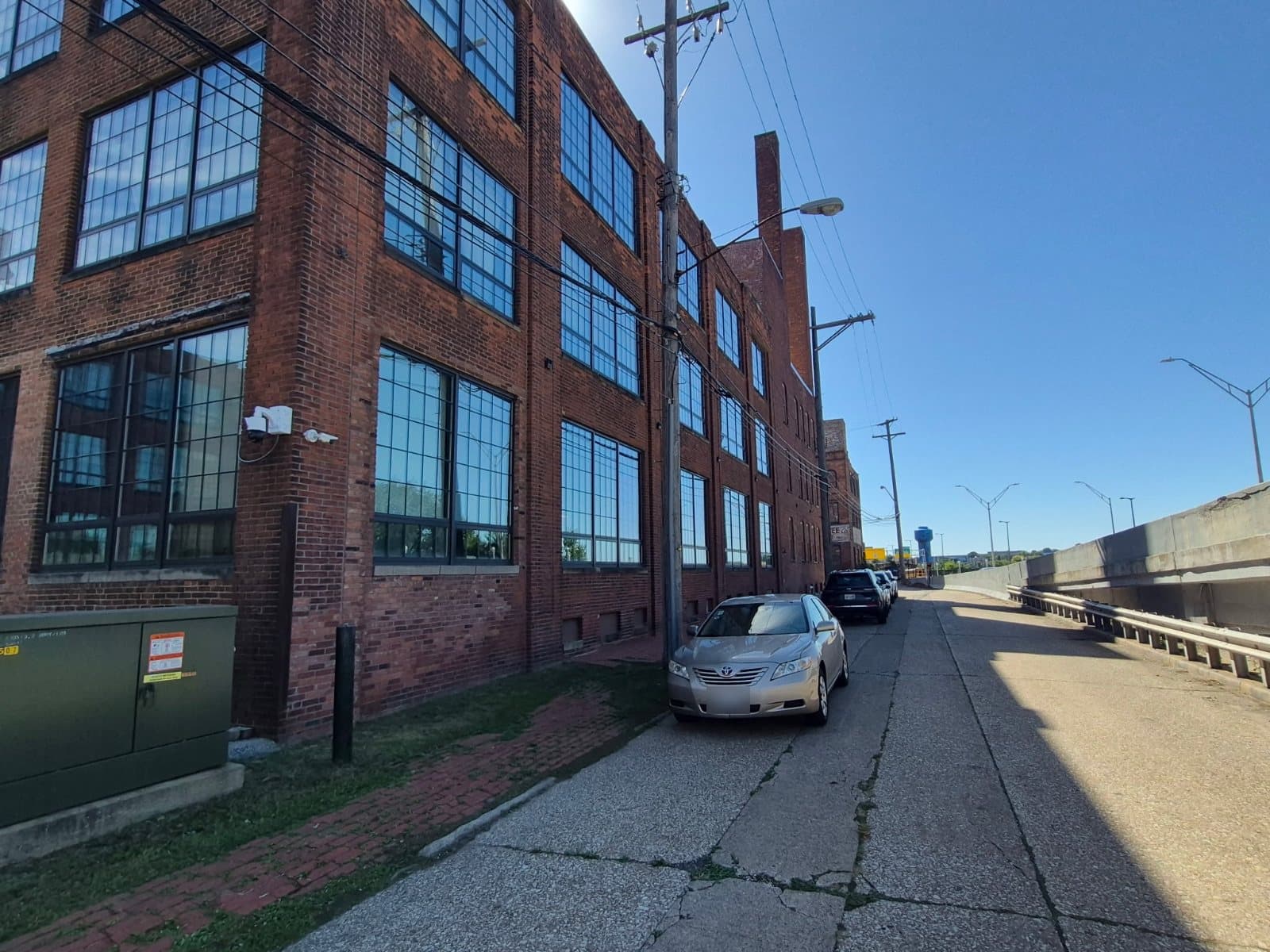 A four-story brick warehouse along the street, large multi-pane windows on every floor, an overpass to the right.