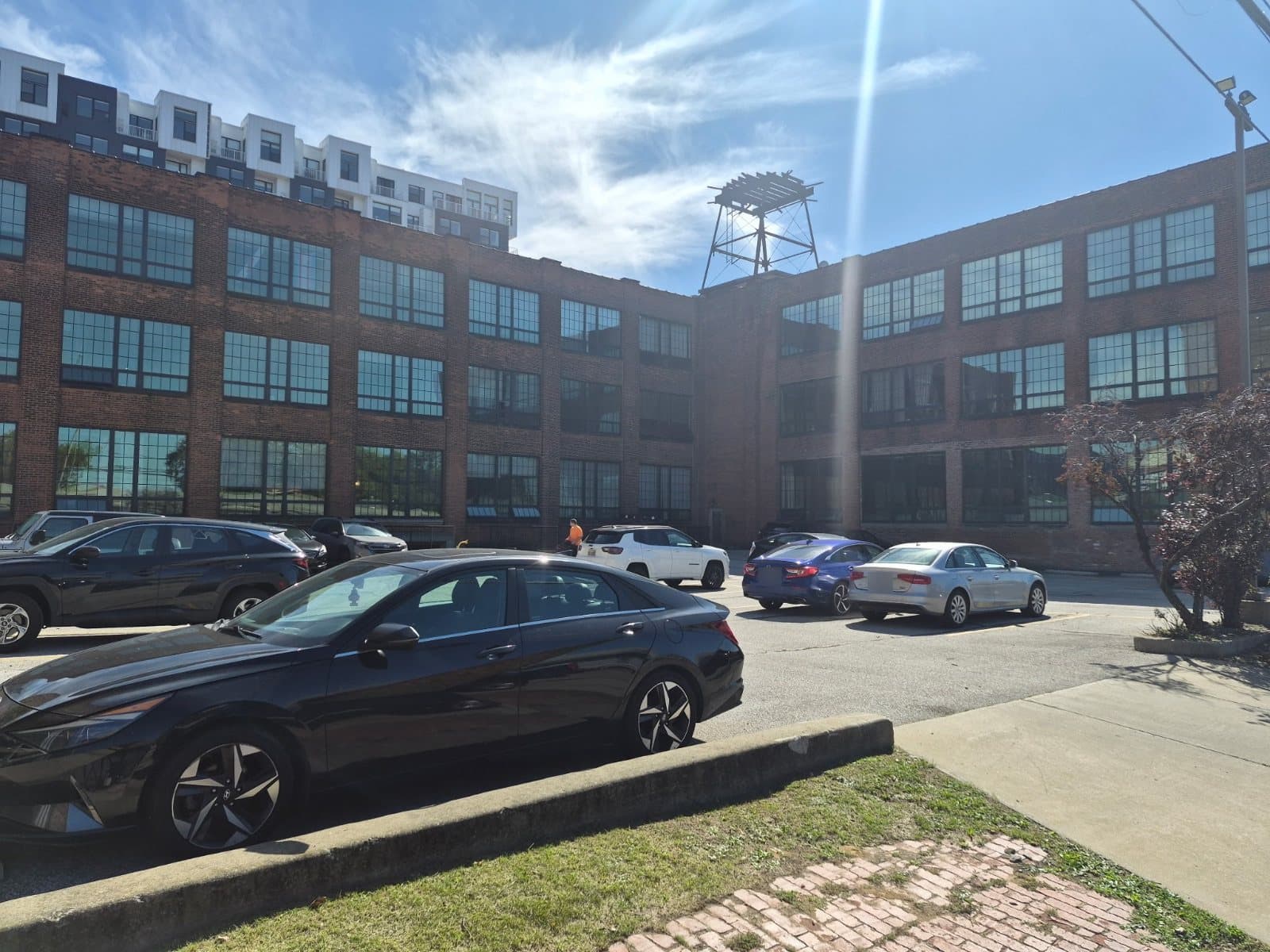 Two wings of a brick warehouse around a parking lot, long runs of gridded windows on three floors.