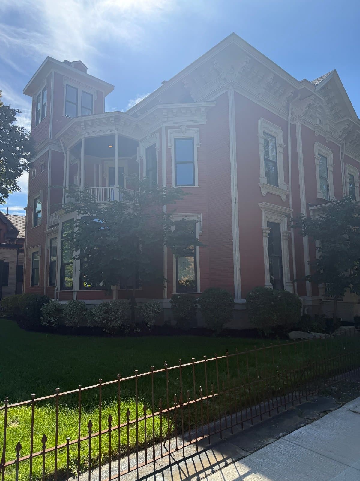 The mansion's corner tower and bay seen from the sidewalk, tall windows with white hoods on each floor.