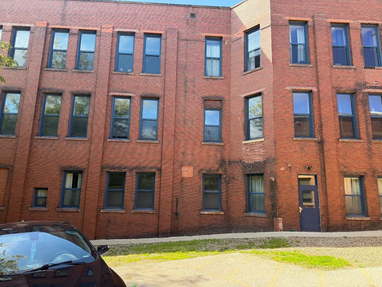 A three-story red brick building with rows of tall double-hung windows in dark blue frames, a blue service door at ground level.