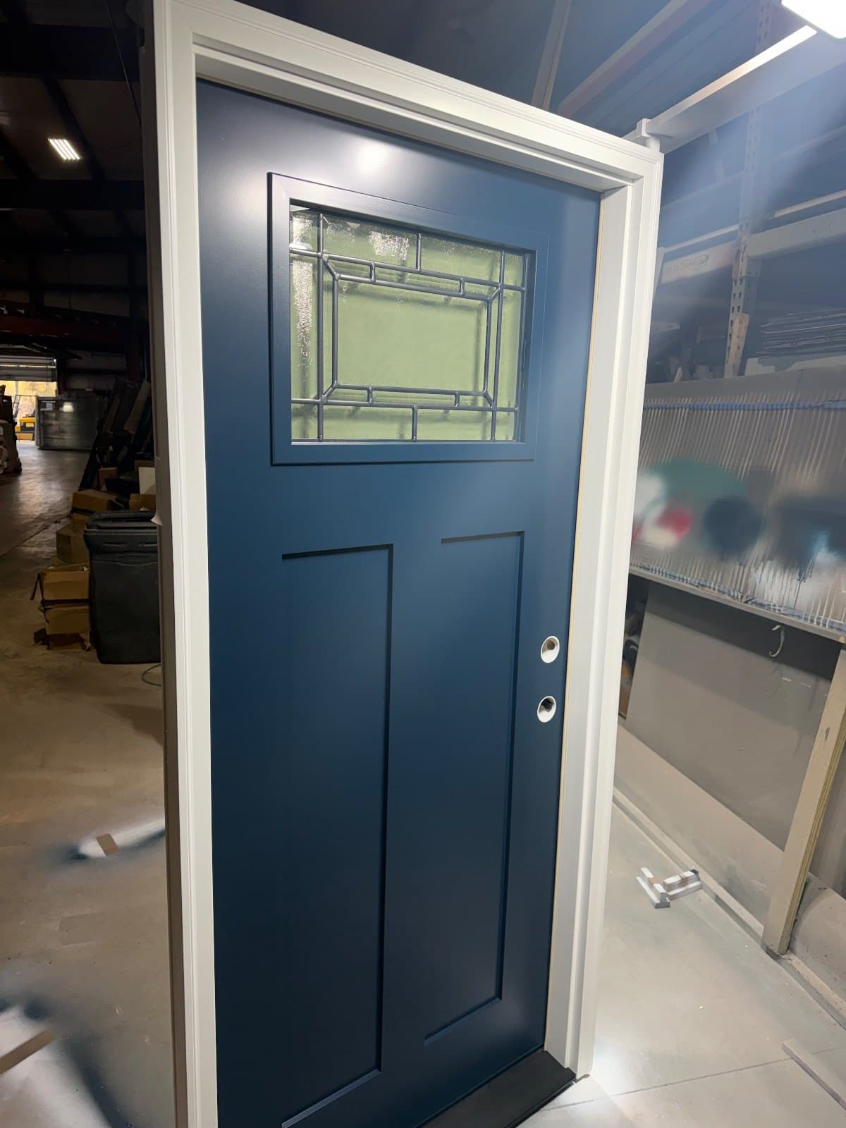 A blue entry door standing in the shop, decorative leaded glass in the upper lite over two flat panels, set in a white frame.