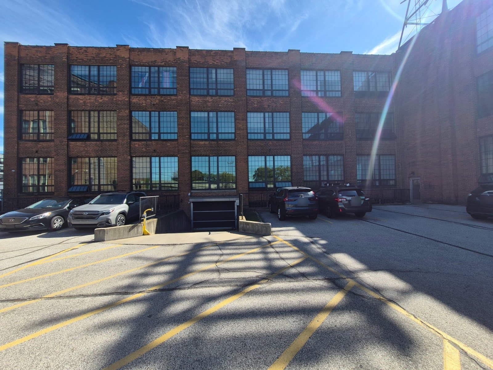 A flat brick elevation of a warehouse, three rows of large gridded windows above a parking lot.
