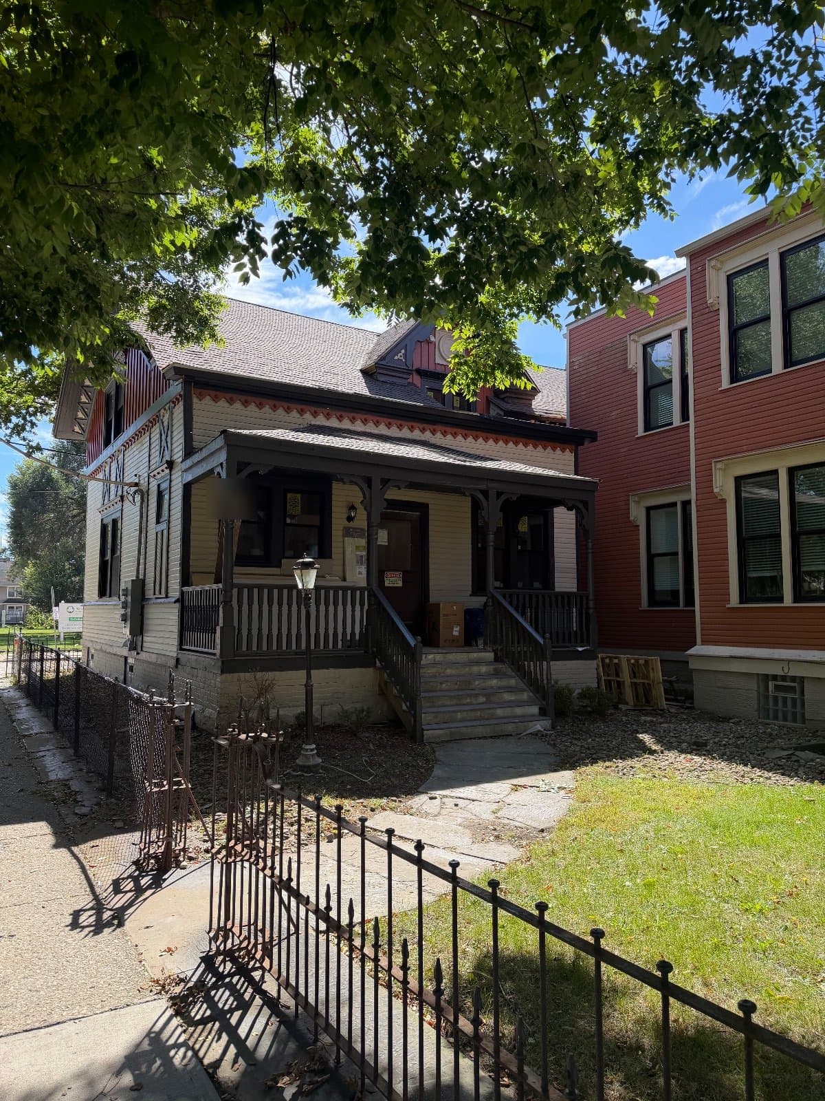 A cream-sided porch wing with dark trim and a covered porch, the red mansion rising beside it.