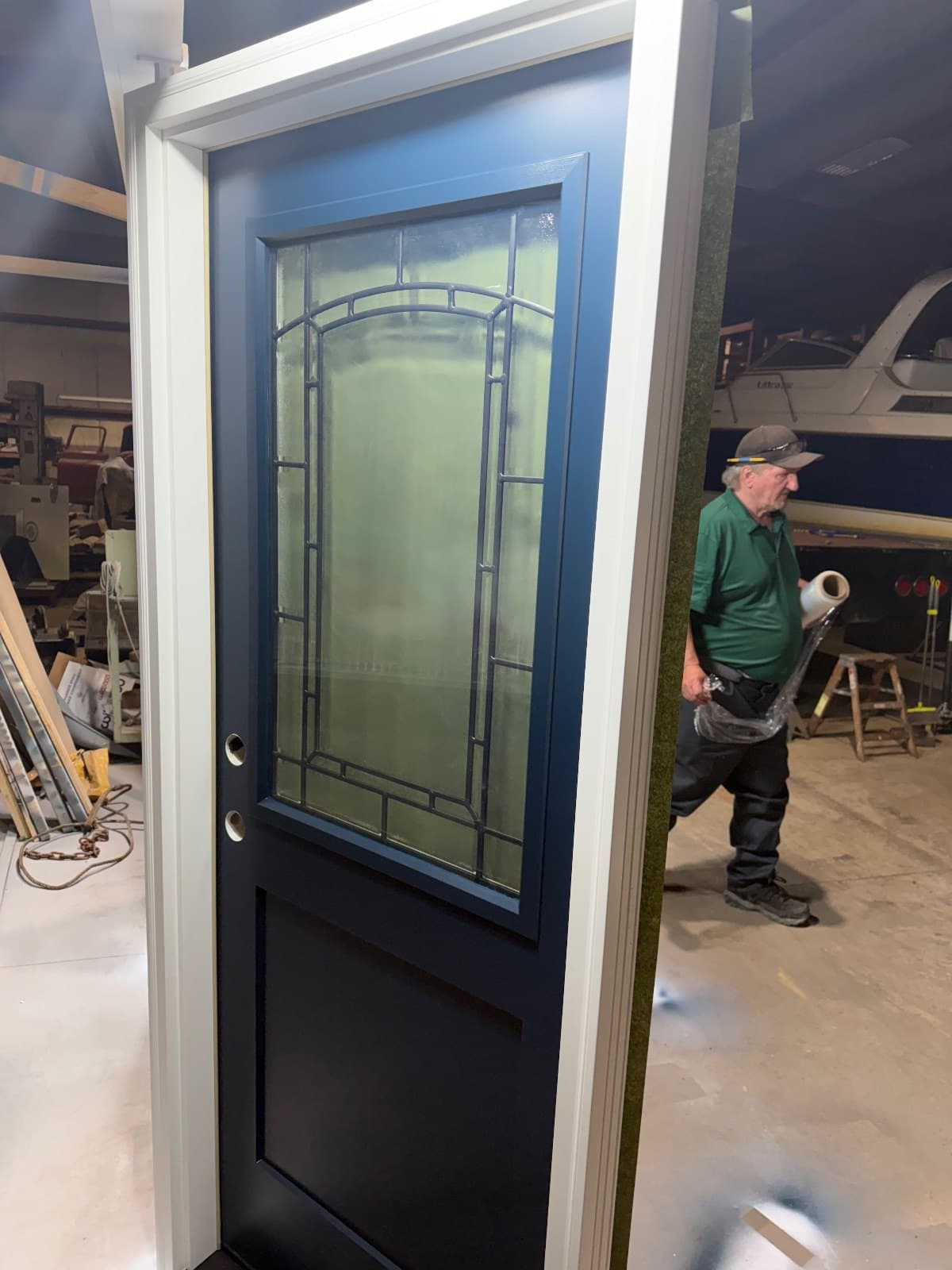 A dark blue entry door in the shop with an arched decorative leaded lite, a man in a green shirt passing behind it.