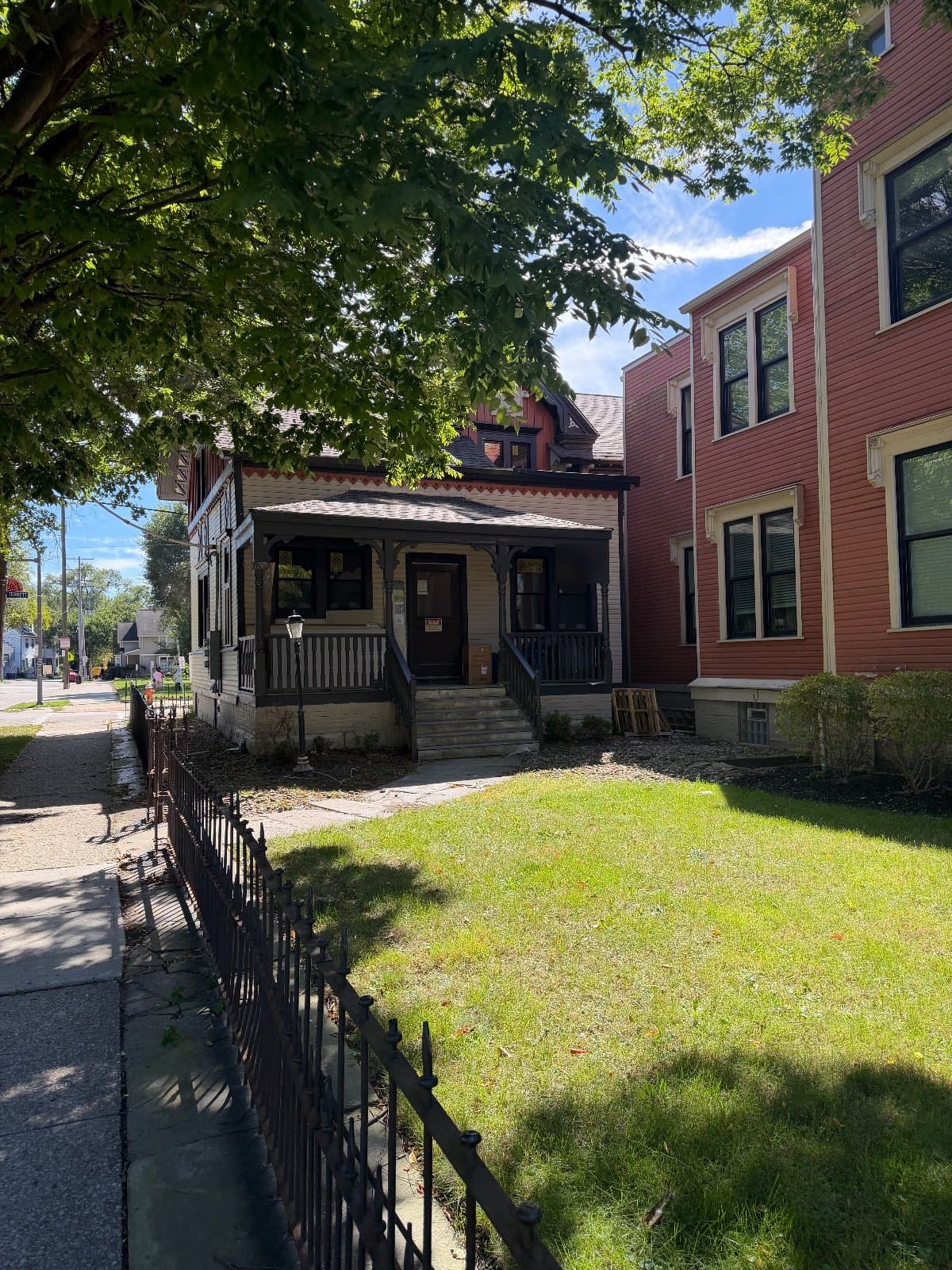 The porch wing and the red mansion from the sidewalk, an iron fence along the lawn.