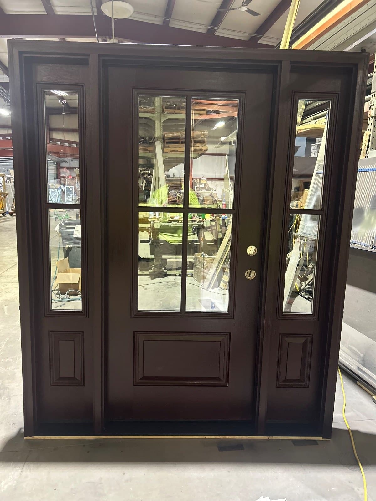 A dark espresso entry door with two matching sidelites, clear beveled glass and brass hardware, standing in the shop.