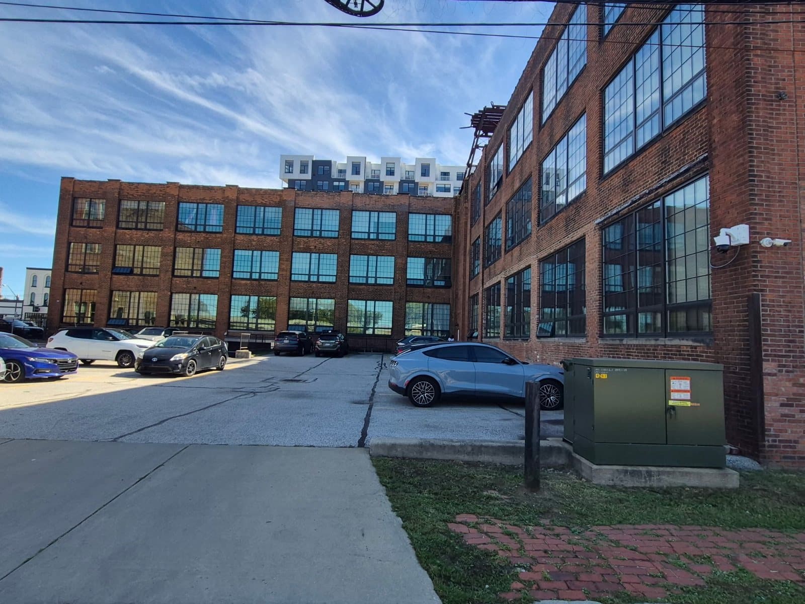 A brick warehouse wing with tall gridded windows on the right, a second wing across the parking lot.