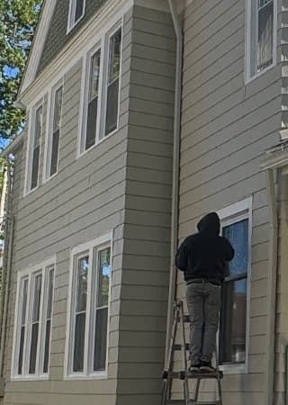 The side wall: paired double-hung windows on two floors, a man on a ladder working at the frame of a window by the downspout.