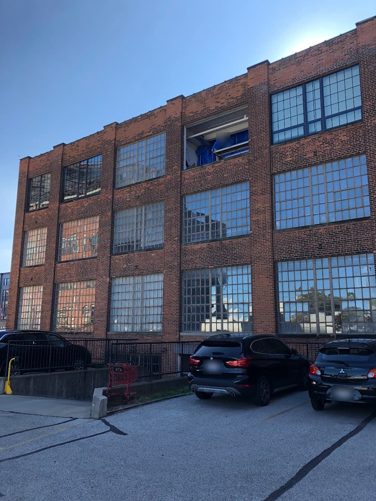 The parking-lot side mid-job: new dark-framed windows across the top floor, one top-floor opening still empty with a crew member and blue tarps inside, the original light steel windows on the floors below.