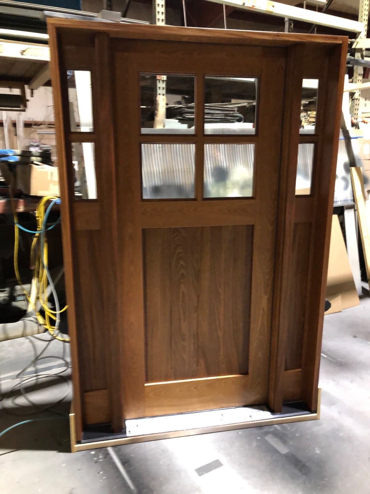 A stained wood craftsman door with a four-lite top over a single wide panel, standing in the shop.