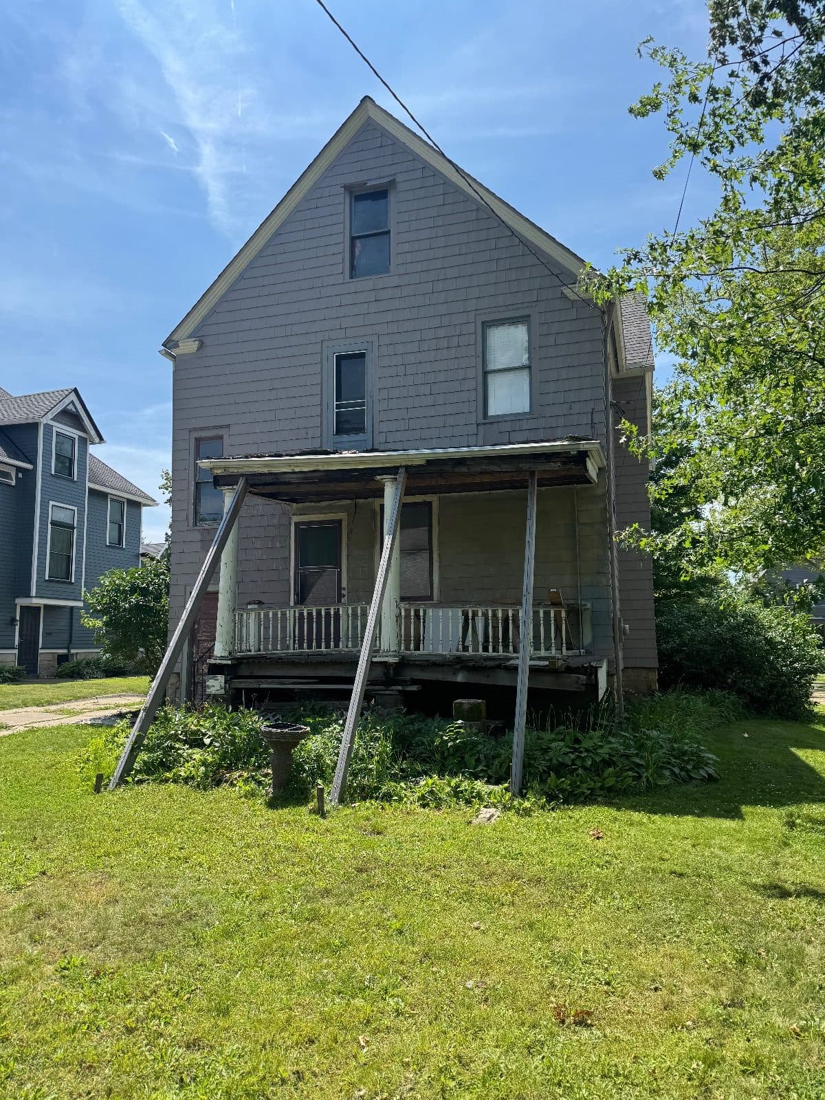 Before: the rear gable straight on, gray clapboard, old windows on three floors over a sagging porch.