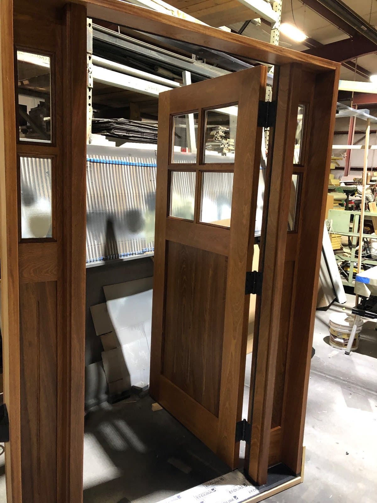 A stained craftsman door and its sidelites standing open at an angle in the shop.