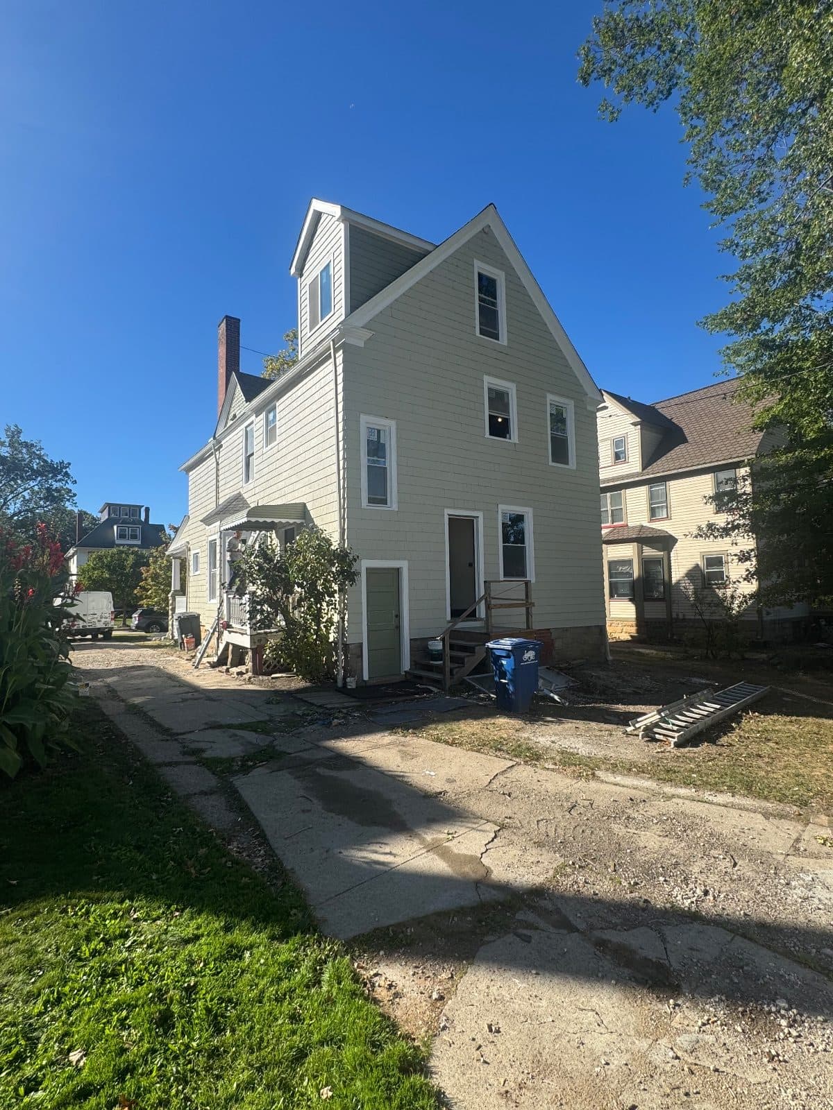 After: the rear of the house in sage siding, the propped porch gone, new white-framed windows on every floor.