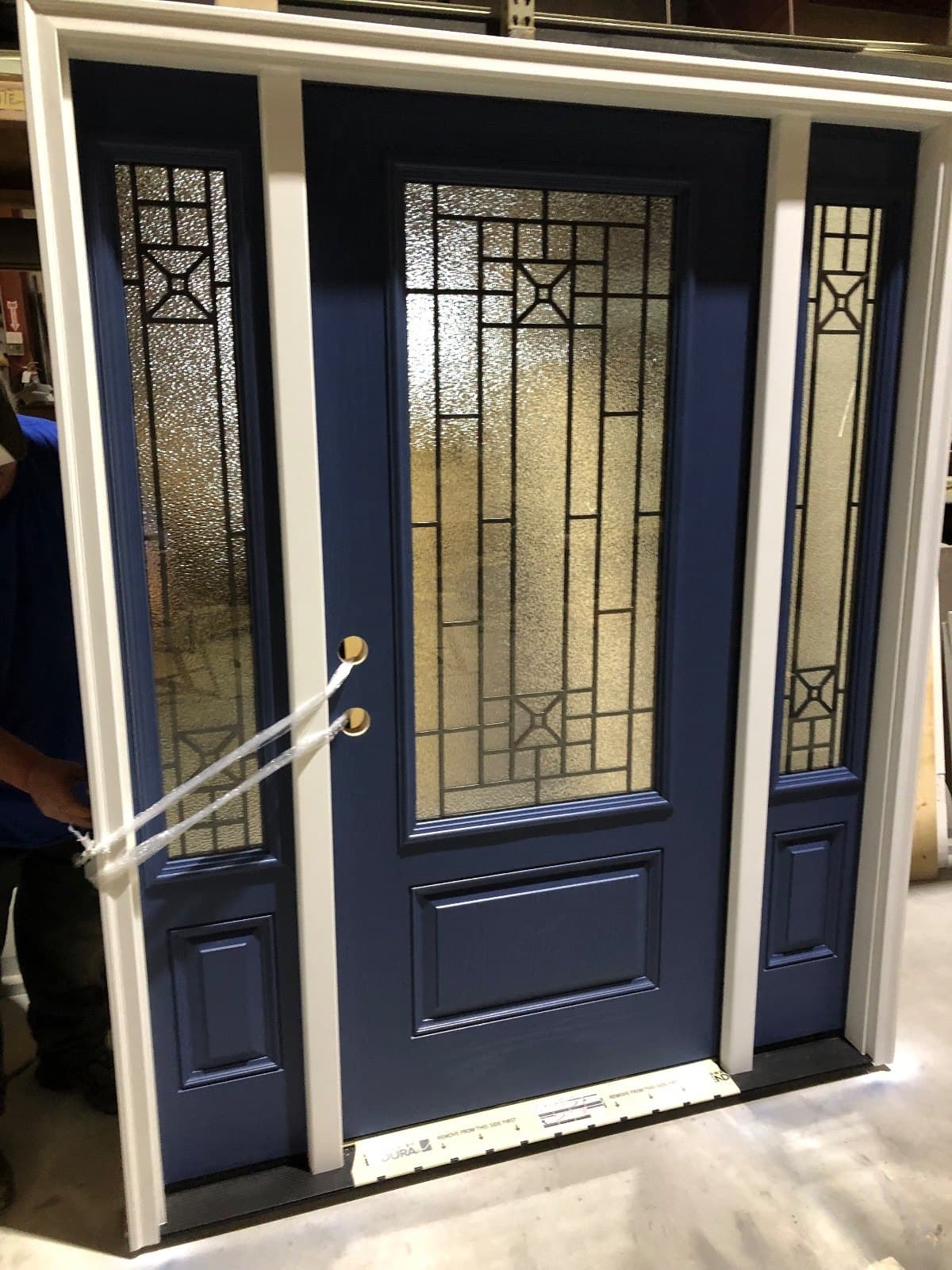 A navy entry door with decorative leaded glass, two leaded sidelites and matching transom lights, standing in the shop.