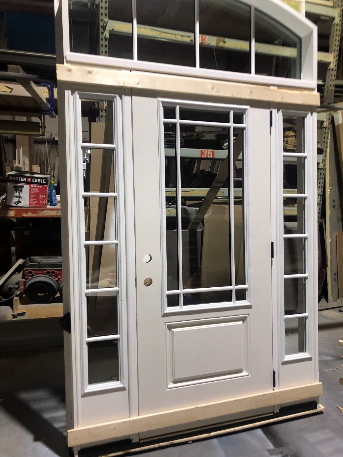 A white door with divided-lite sidelites and an arched transom over the whole unit, standing in the shop.