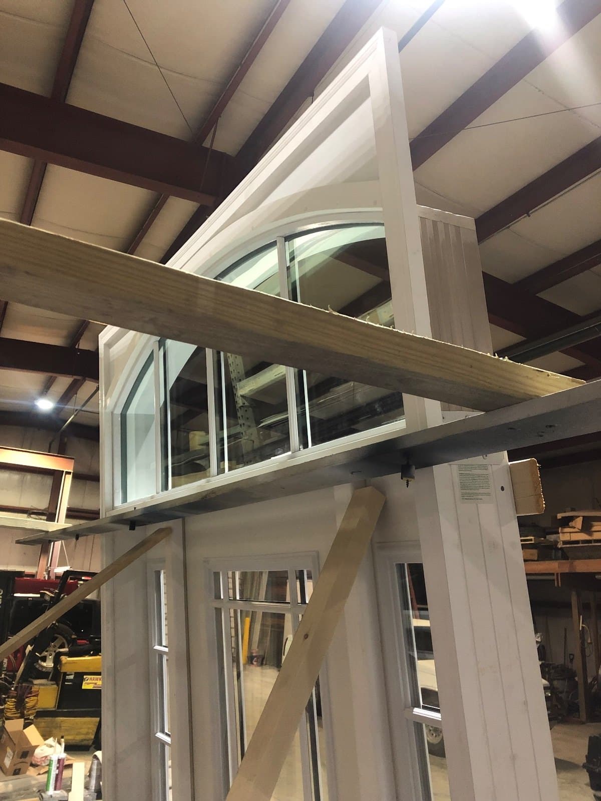 A tall white door unit with a curved transom above, braced upright under the shop roof.