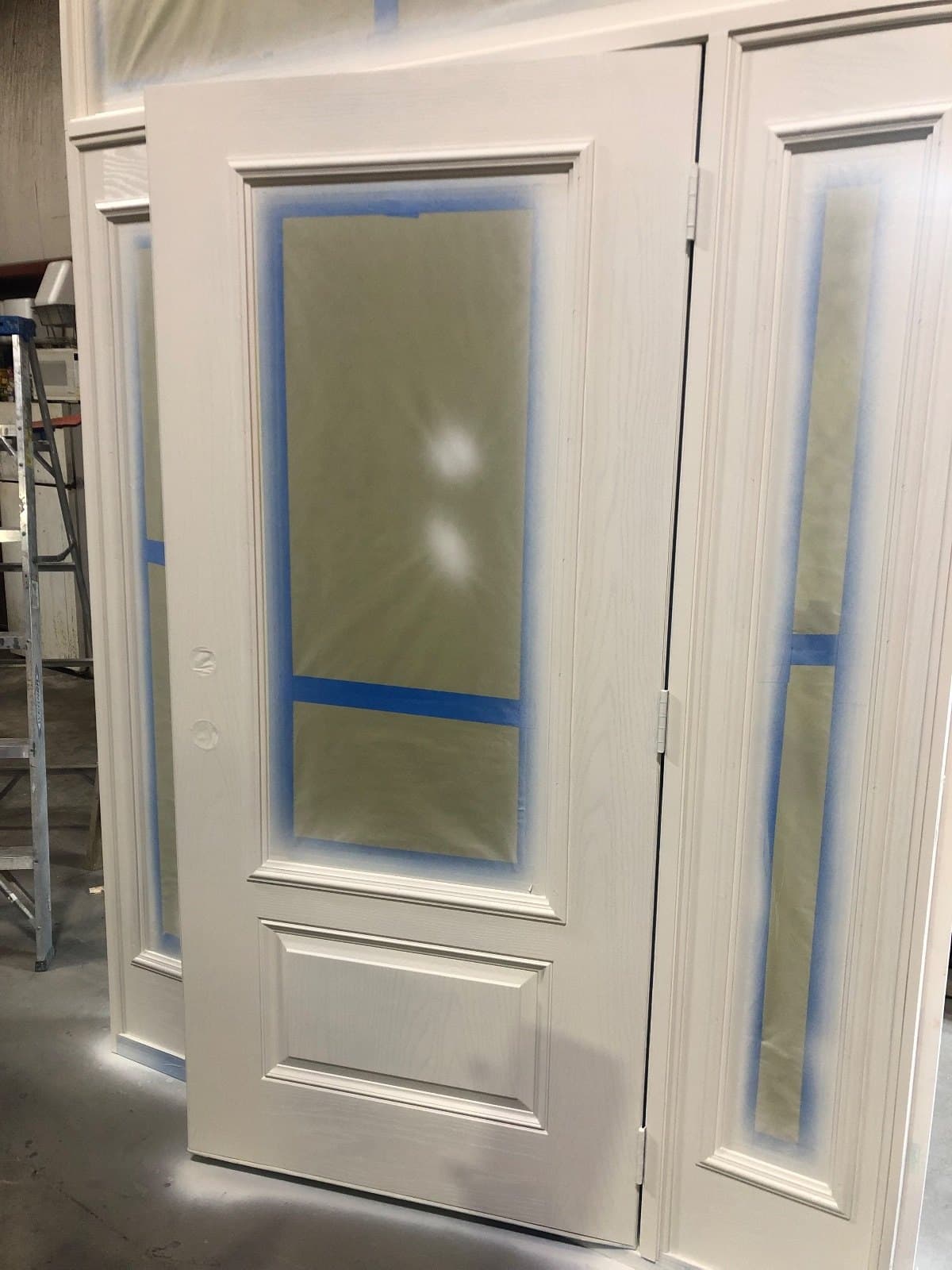 A white entry door with frosted glass and a matching sidelite, glass still taped, in the shop.