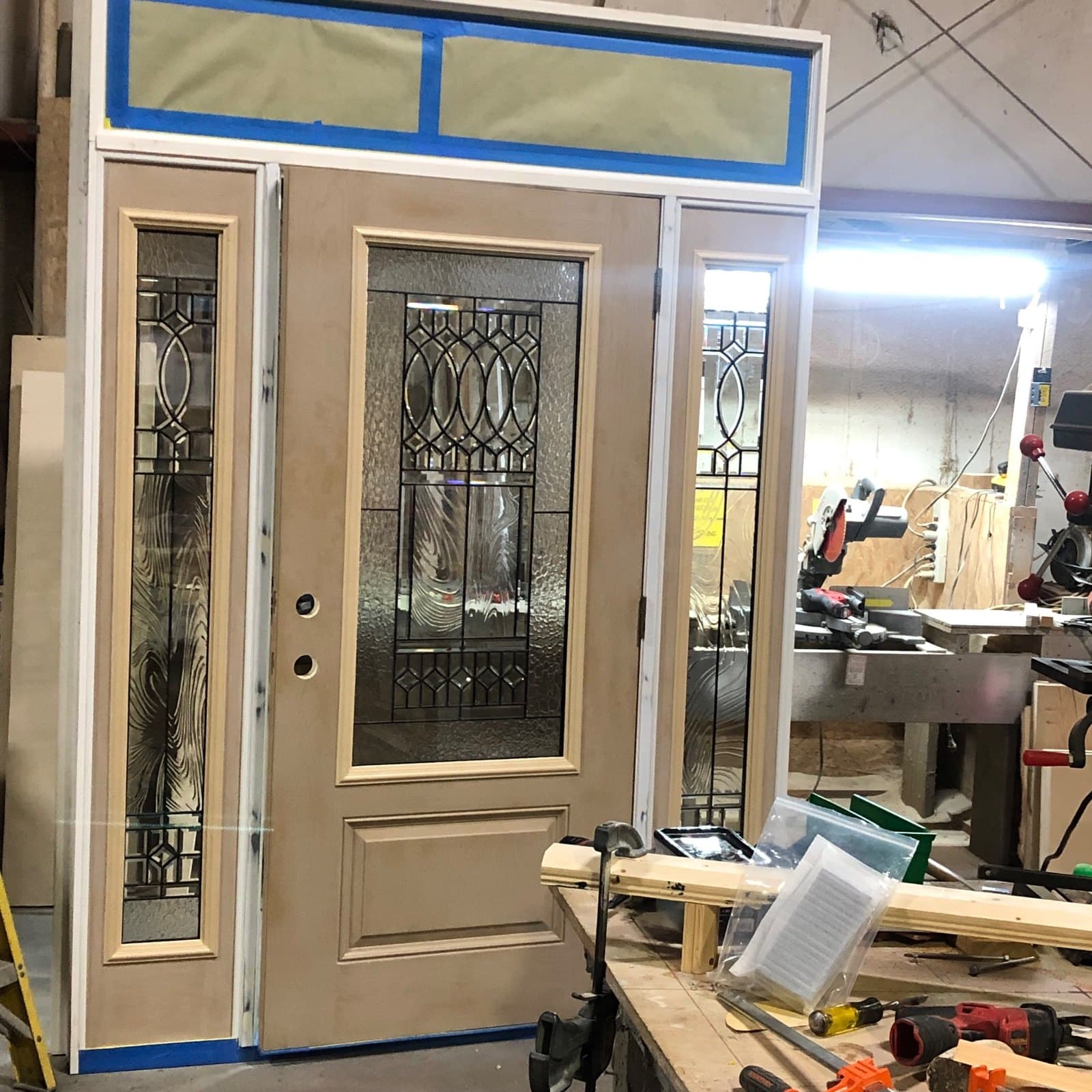 A cream entry door with decorative leaded glass, two leaded sidelites and a taped transom, on the bench.
