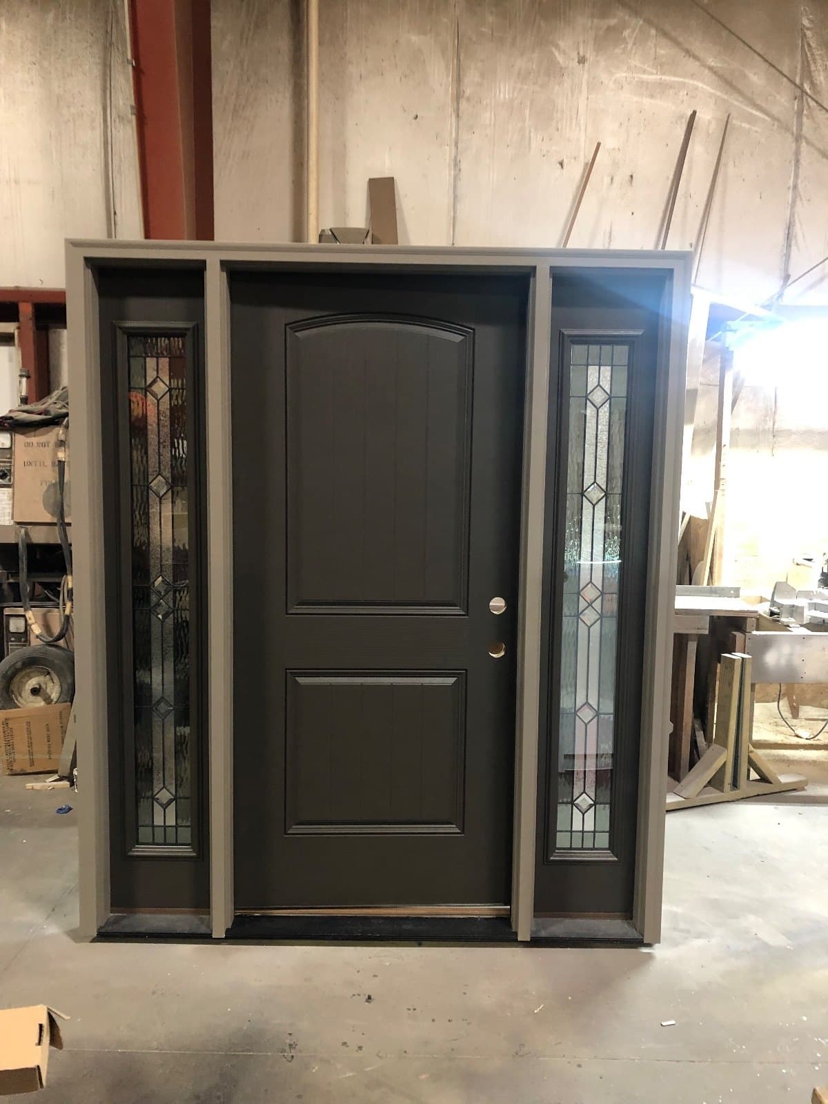A brown entry door between two narrow decorative leaded sidelites, standing in the shop.