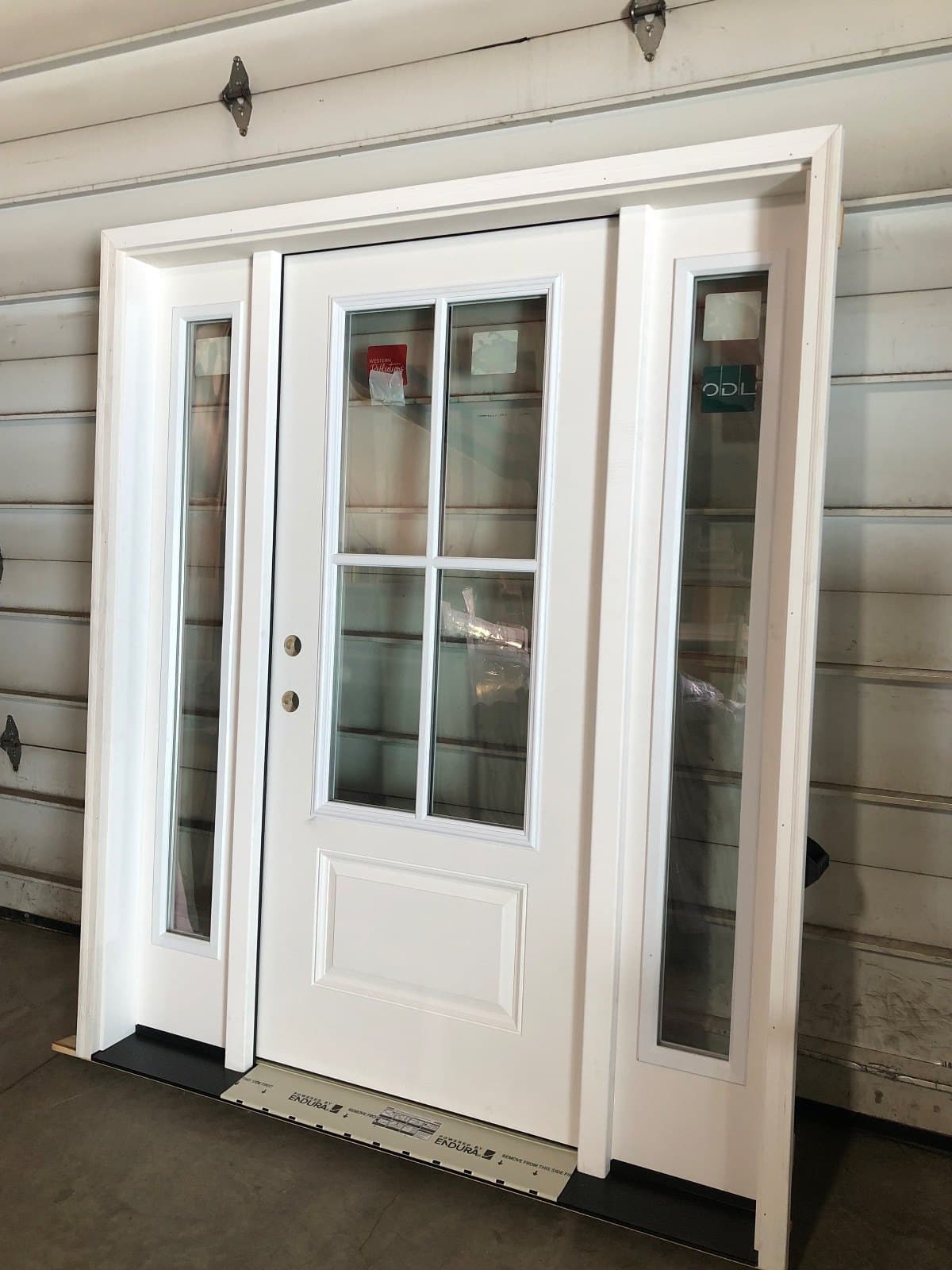 A white entry door with two sidelites in place on a white-sided house.
