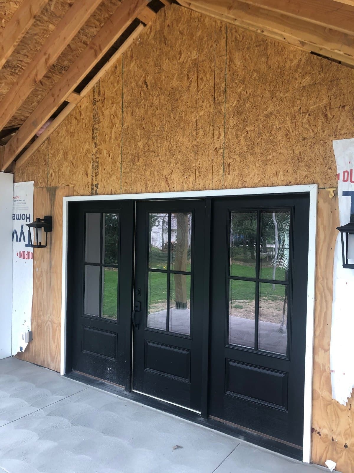 Black double doors with divided lites in a covered porch opening, walls still unfinished.