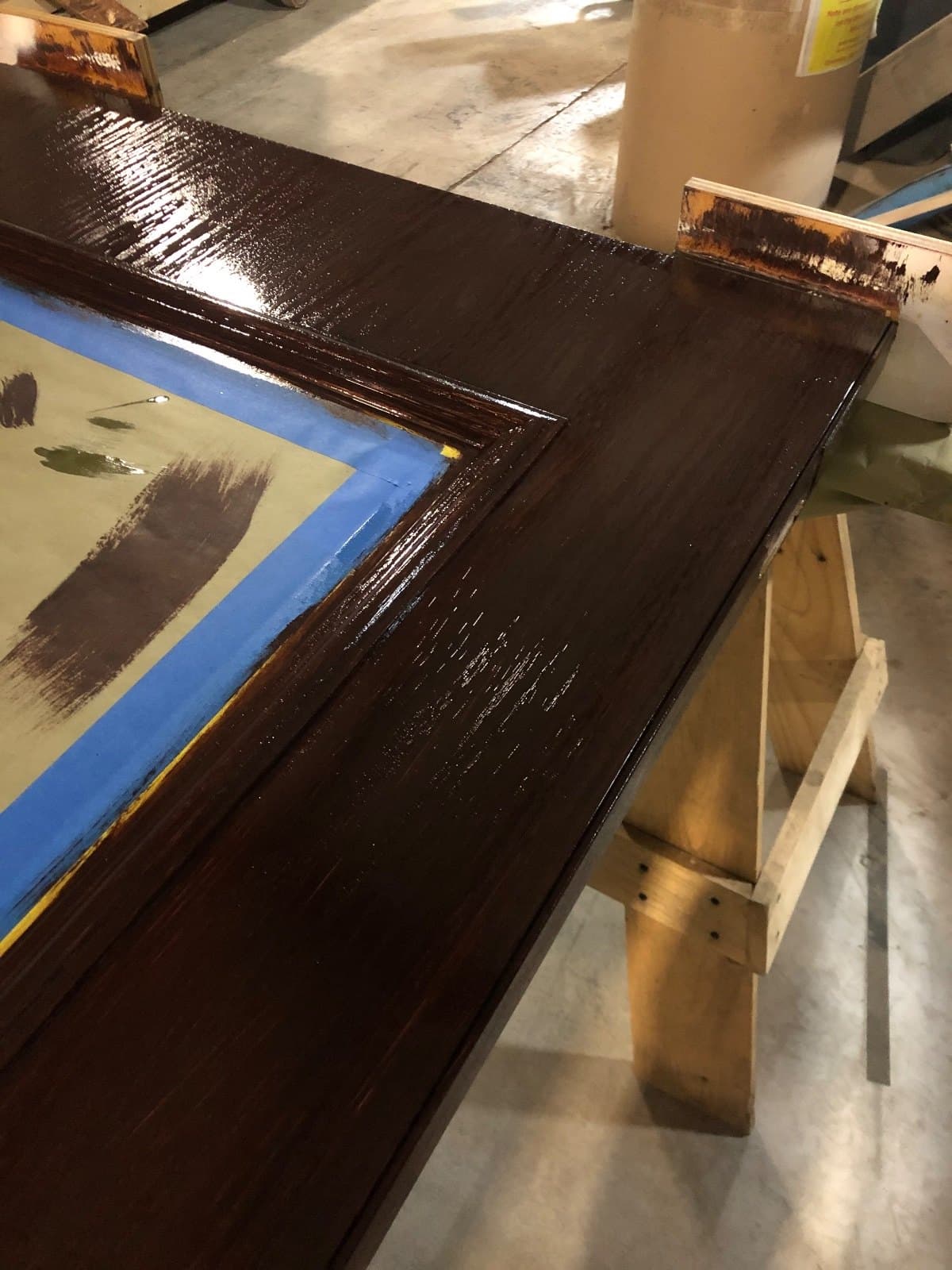 Close view of a door frame in fresh dark stain, masking tape still on the glass.