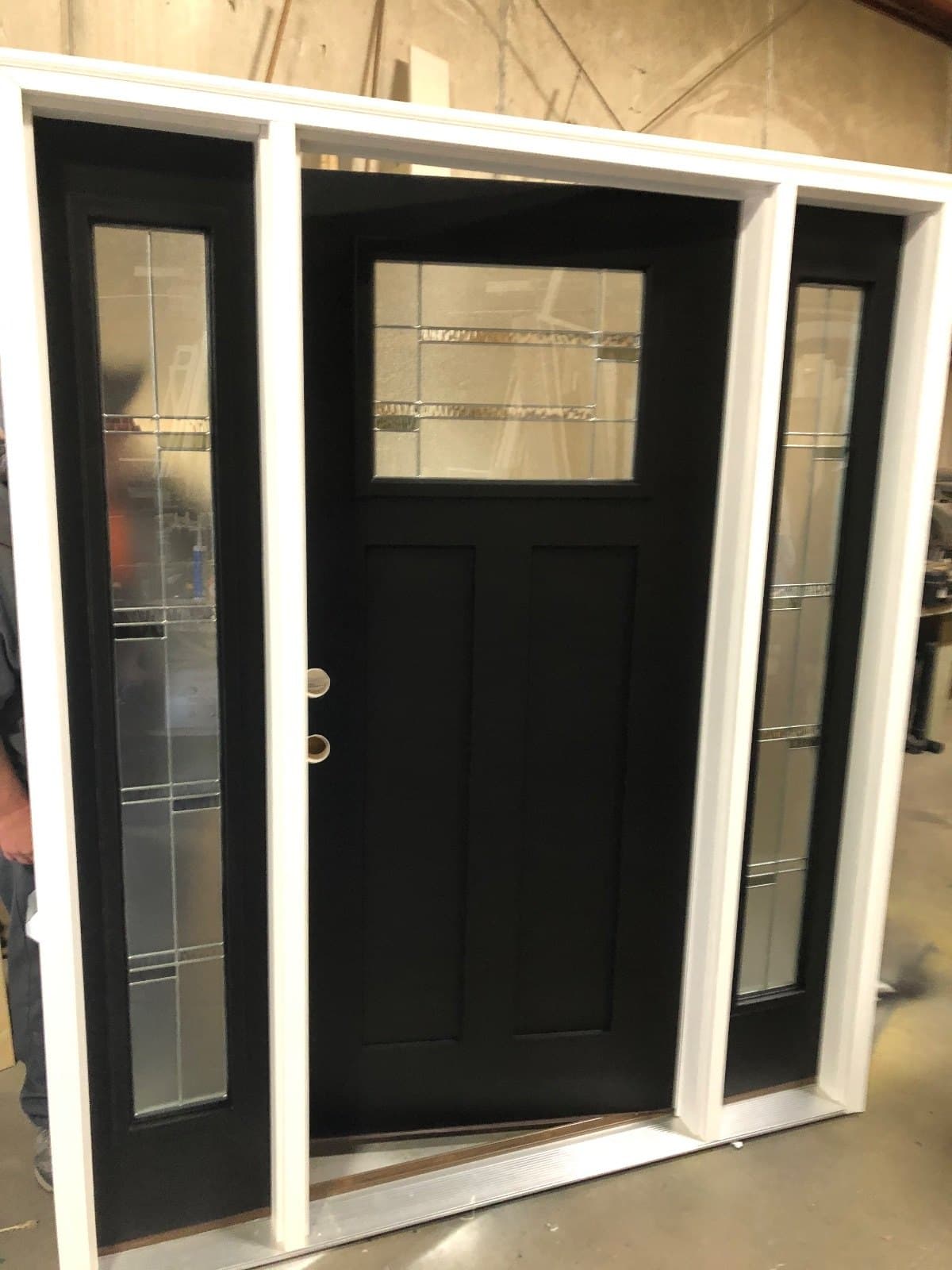 A black craftsman entry door with two divided-lite sidelites, standing in the shop.