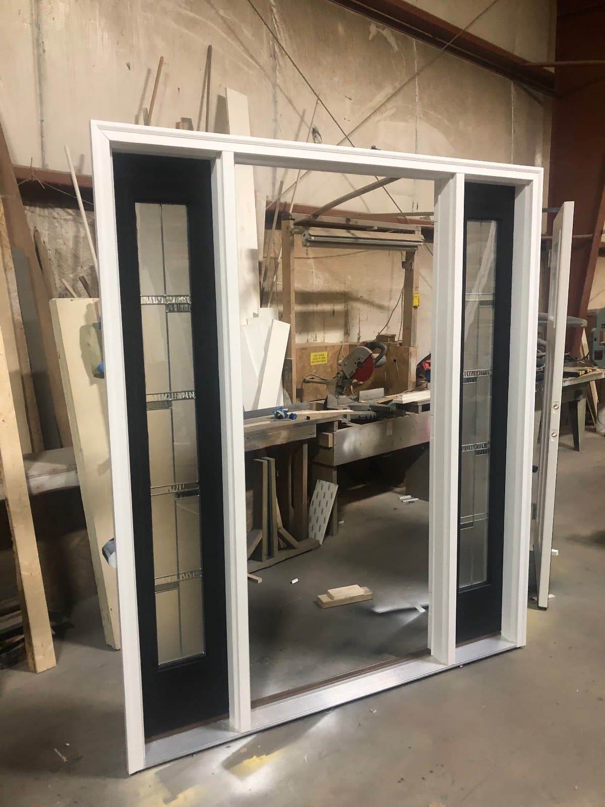 A white entry door with divided-lite sidelites each side, standing in the shop.