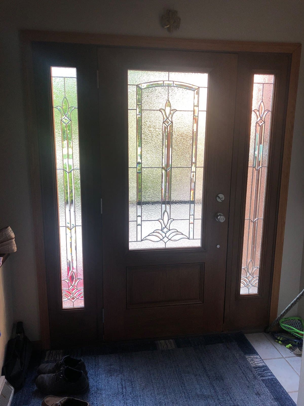 A stained wood entry door with decorative leaded glass and two leaded sidelites, seen from inside the house.
