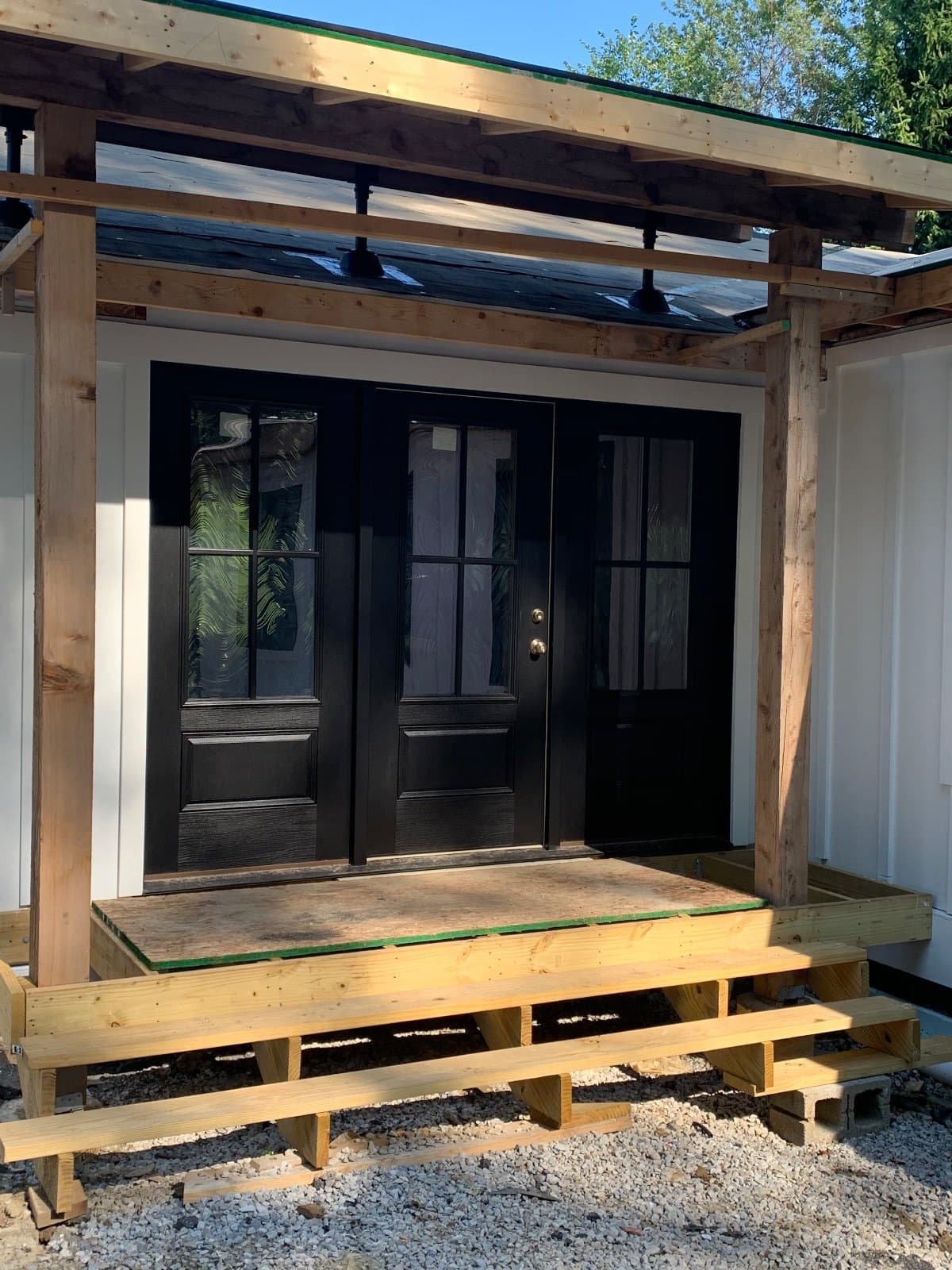Dark double doors with divided lites under a timber porch on a building still under construction.