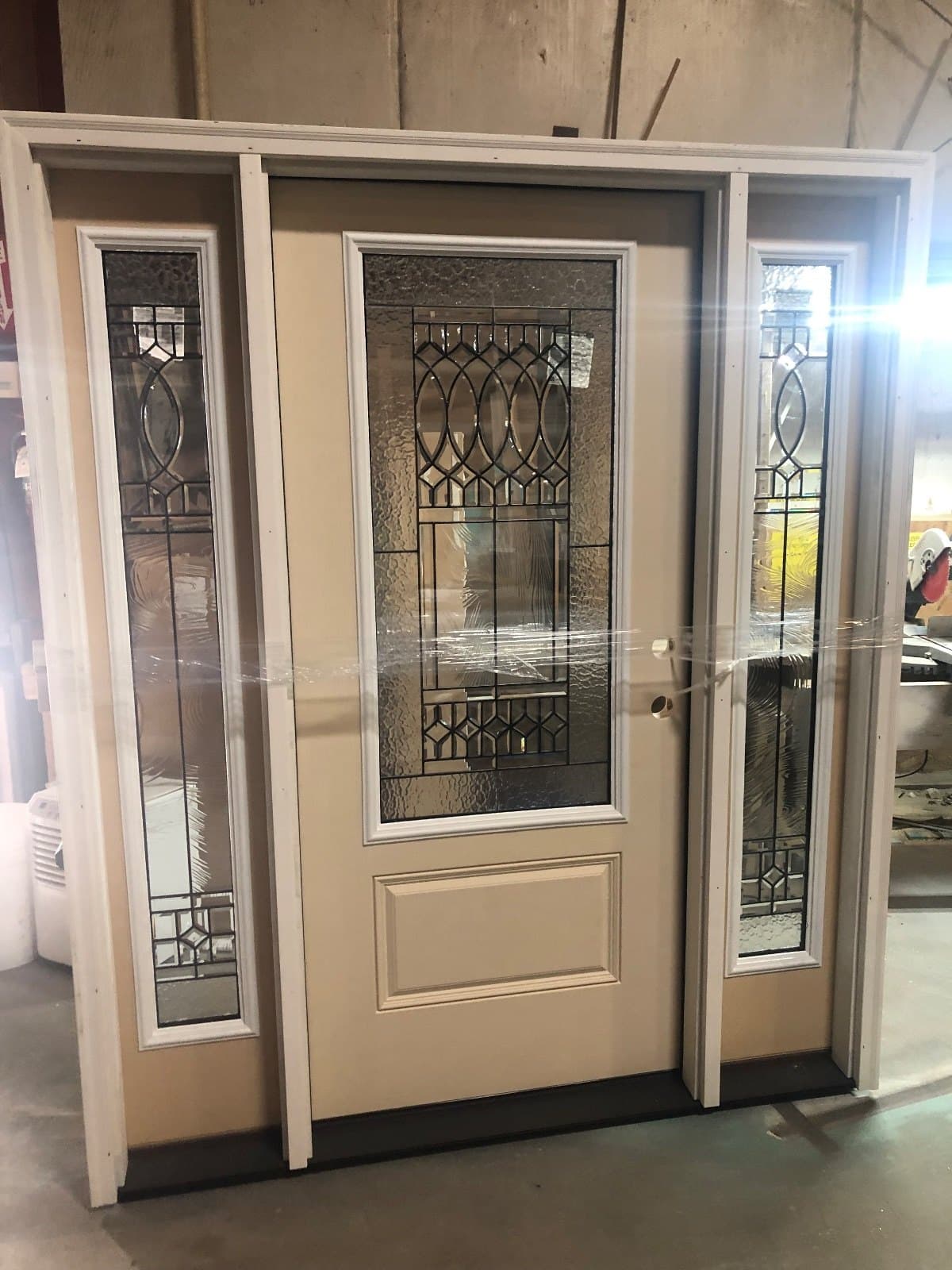 A cream entry door with decorative leaded glass and two matching leaded sidelites, standing in the shop.