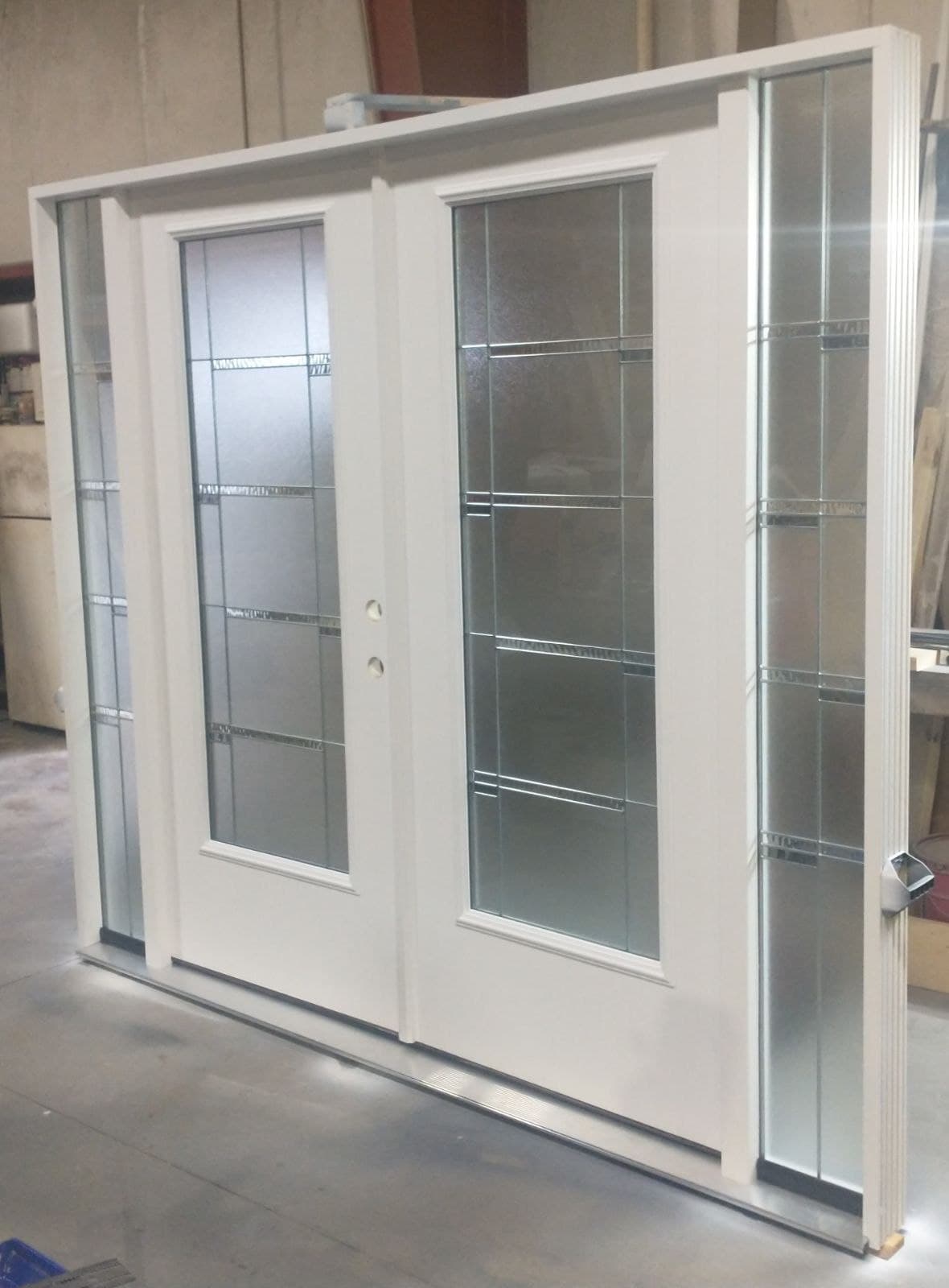 A white double entry door with decorative caming in the glass and matching sidelites, standing in the shop.