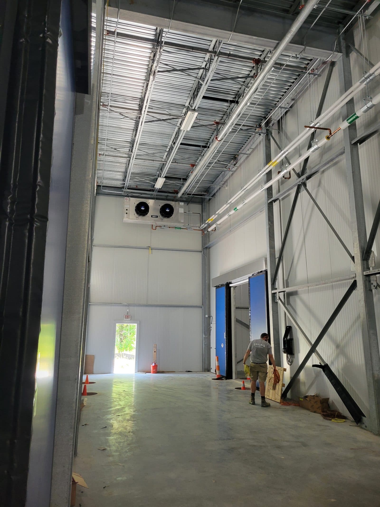 Cooler vestibule with insulated panel walls, evaporator units overhead and an open doorway toward the freezers.