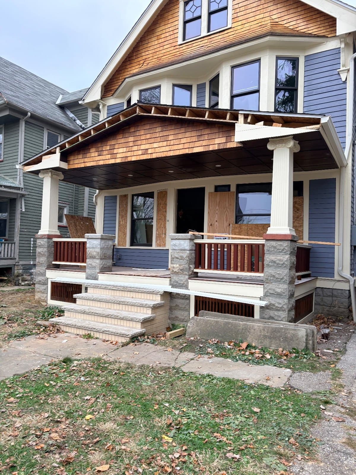 A porch under construction on a house front, new posts and railing, windows in behind.