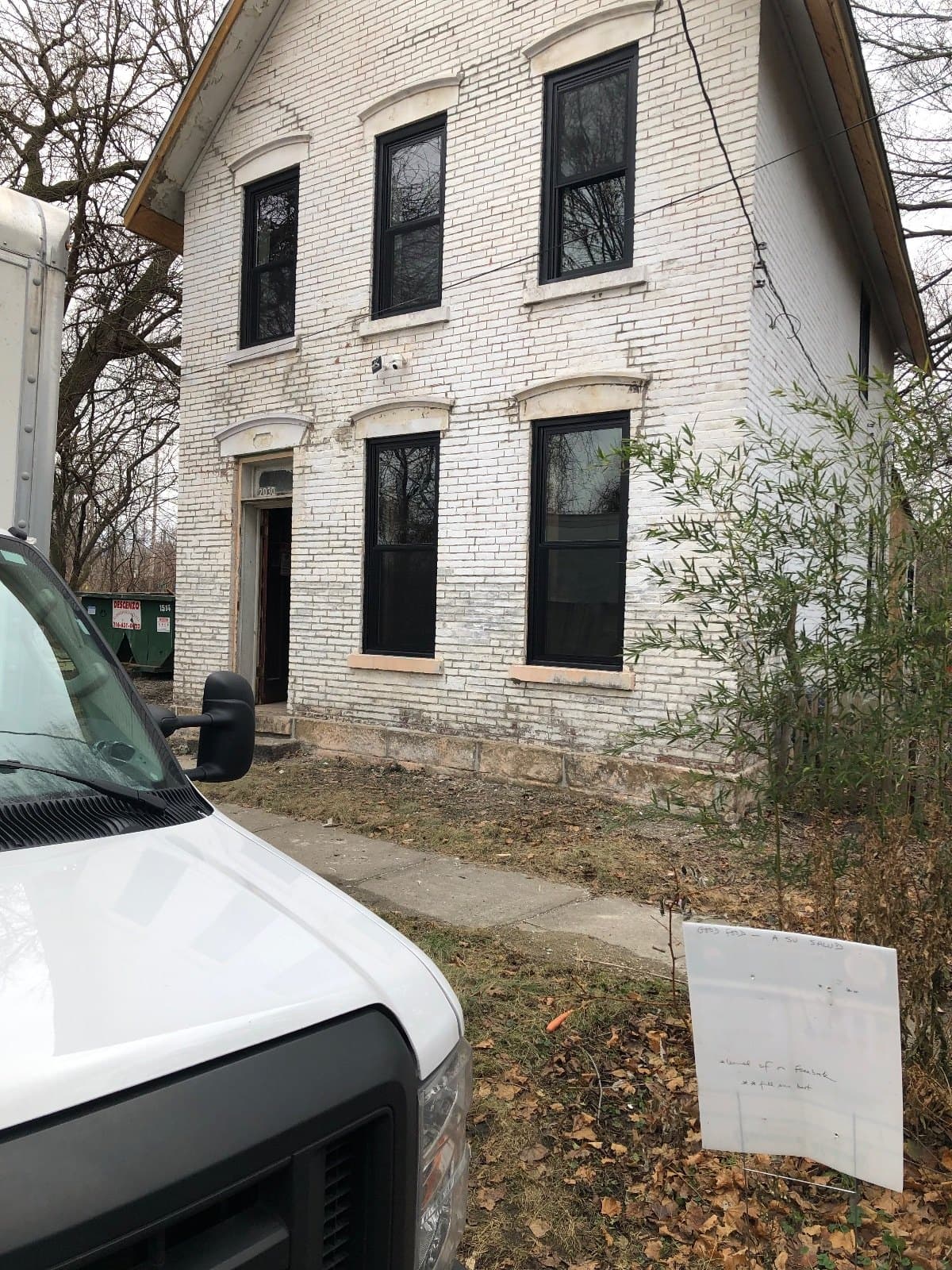 A house with new windows in, a work van parked at the curb and material on the ground.