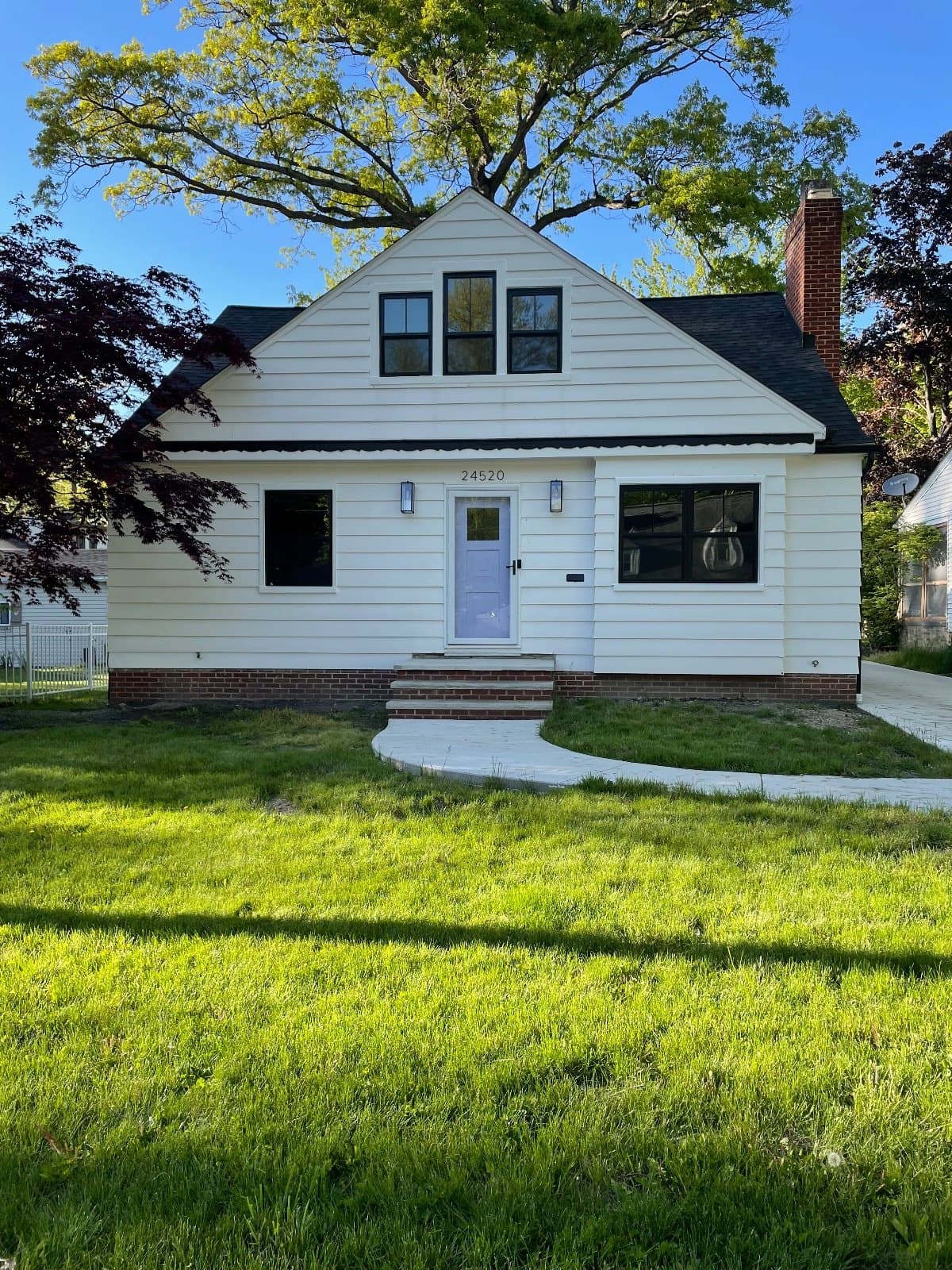 A finished cape-style house in white siding, lawn to the street.