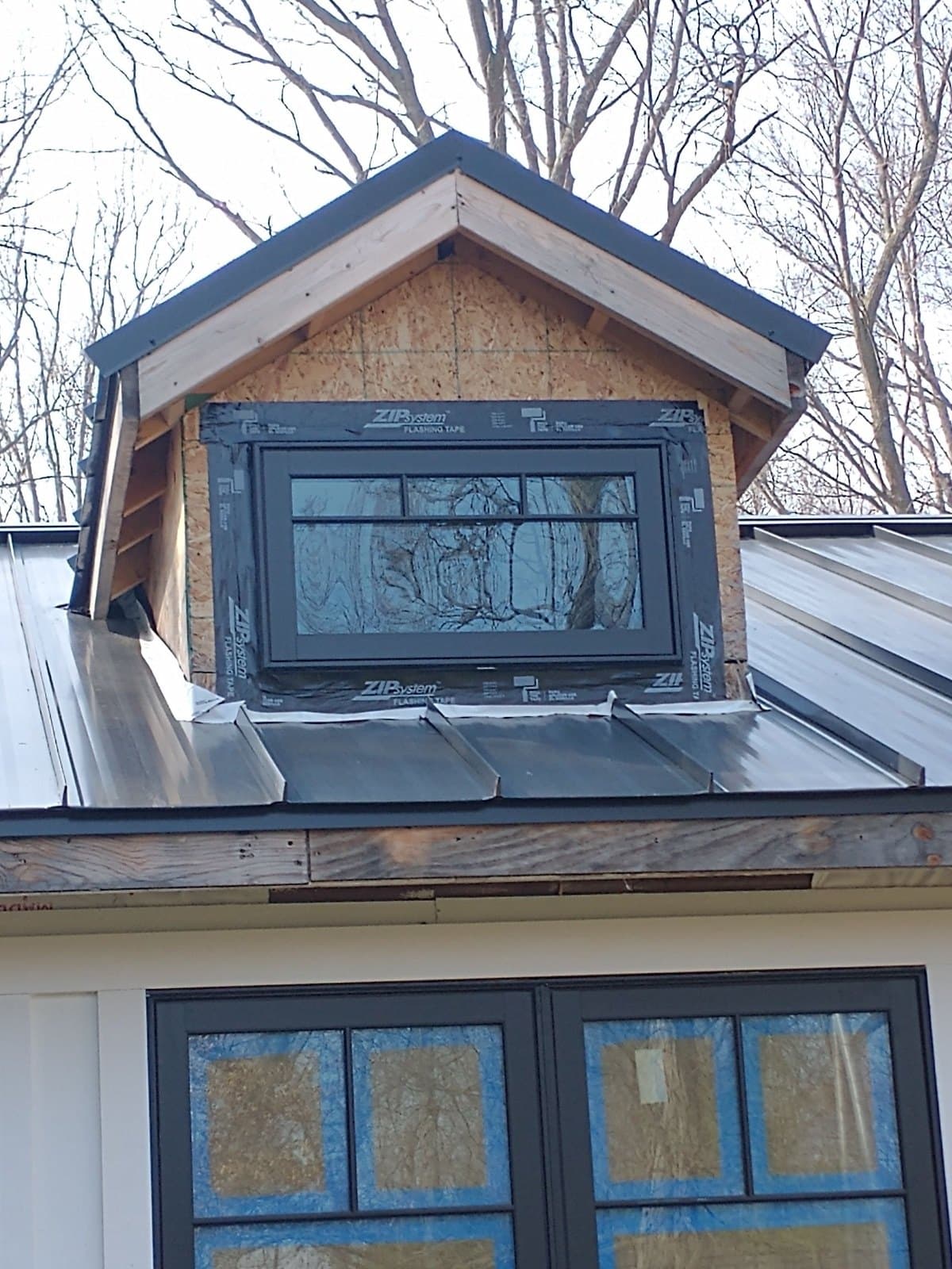 A dormer under construction on a standing-seam roof, window openings taped.