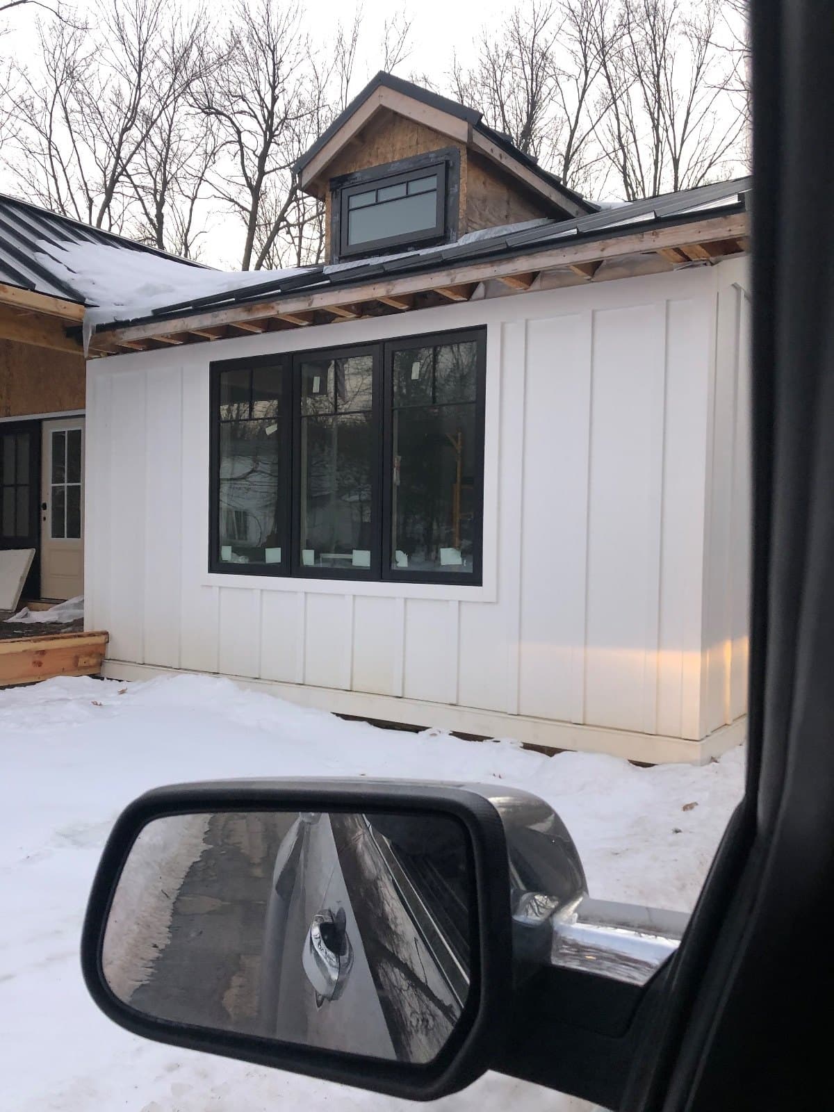 A house with new windows seen past the mirror of a truck parked on the job.