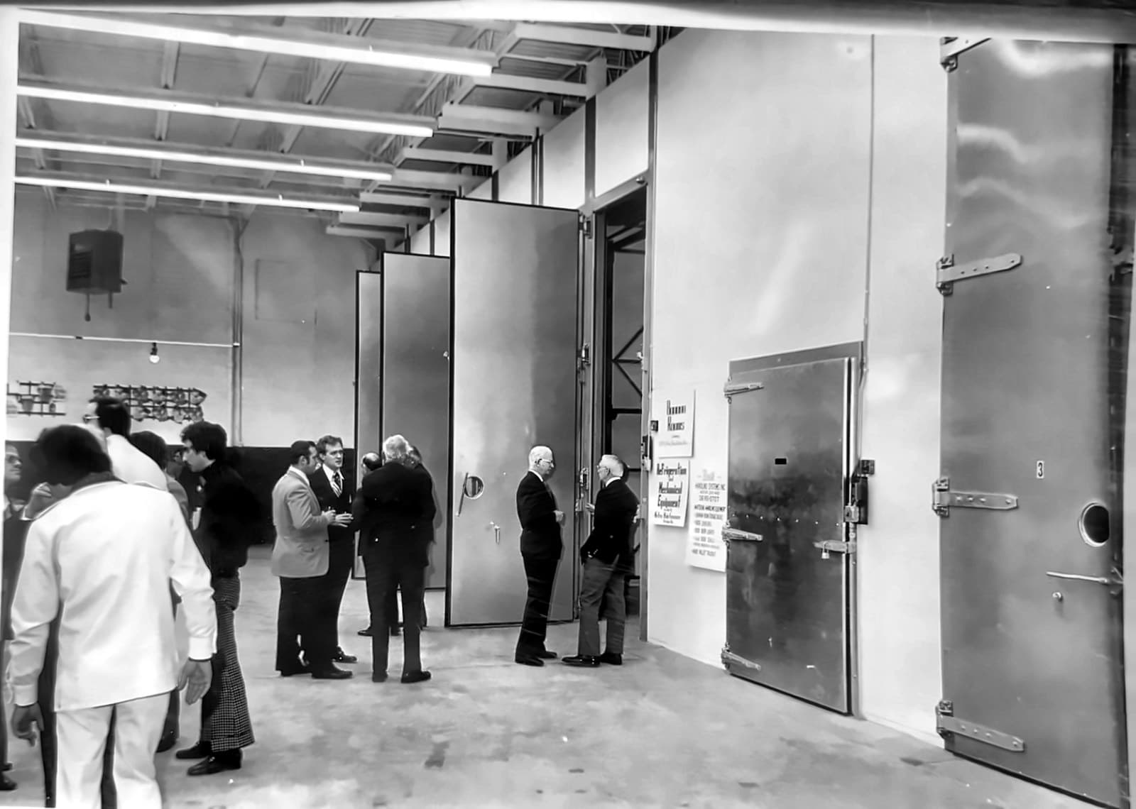 Cold-storage doors along a plant wall on opening day, men in suits gathered by the open doors.