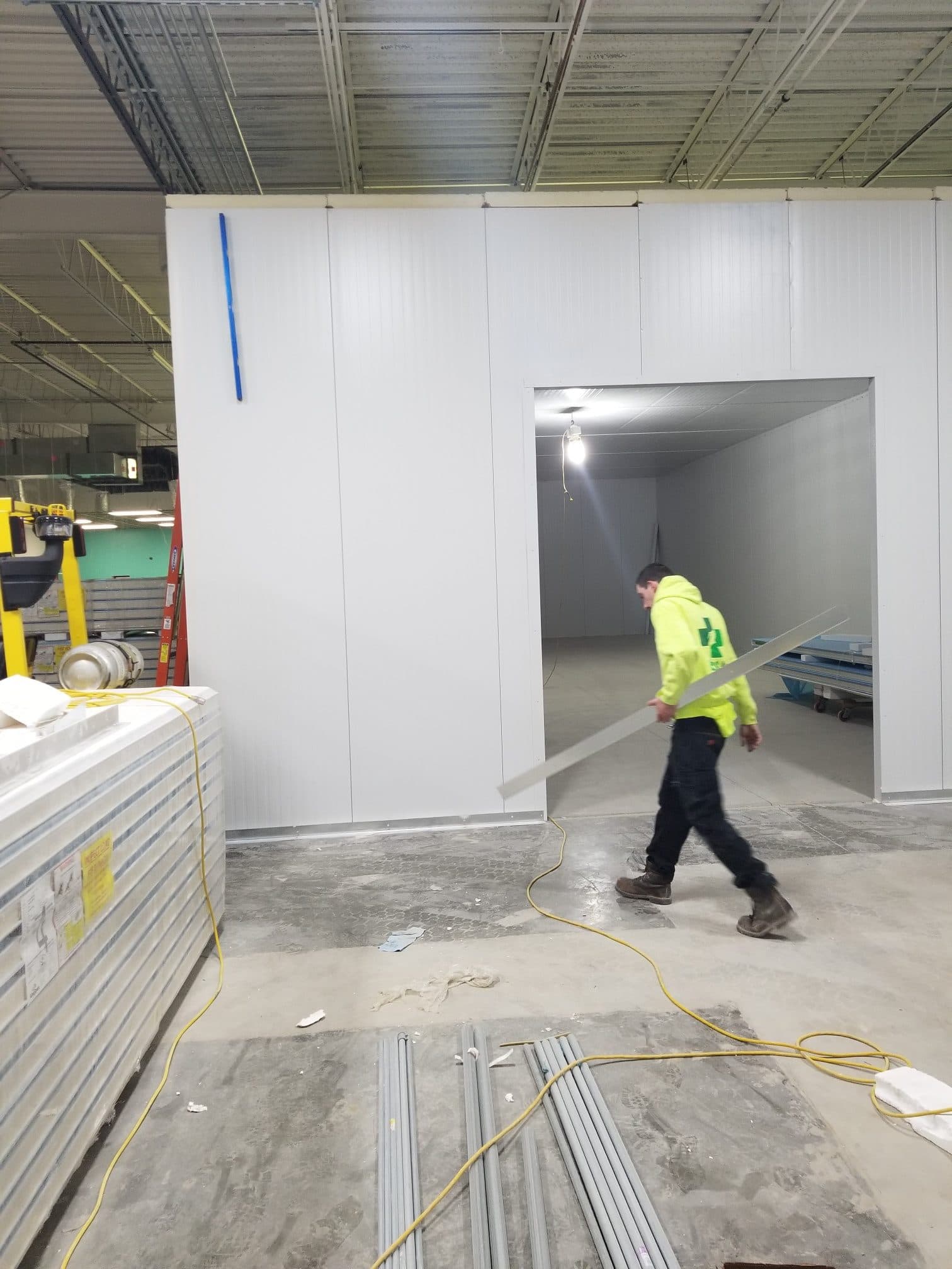 Freezer panel wall with a door opening, panels stacked on the floor, an installer walking past.