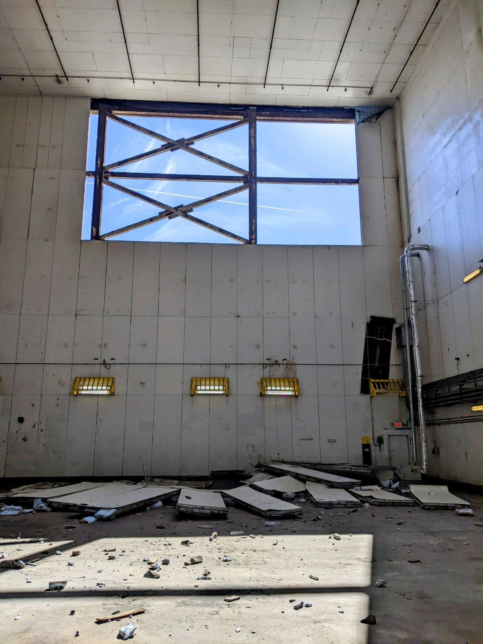 A freezer wall with panels torn out of the upper bay, open sky and structural steel visible through the gap, panel debris across the floor below.
