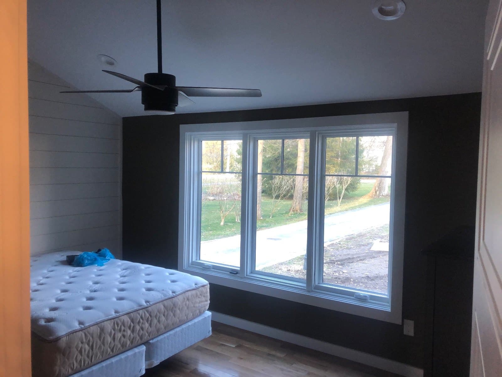 A bedroom with a bare mattress on the floor, a wide three-pane window and finished hardwood.
