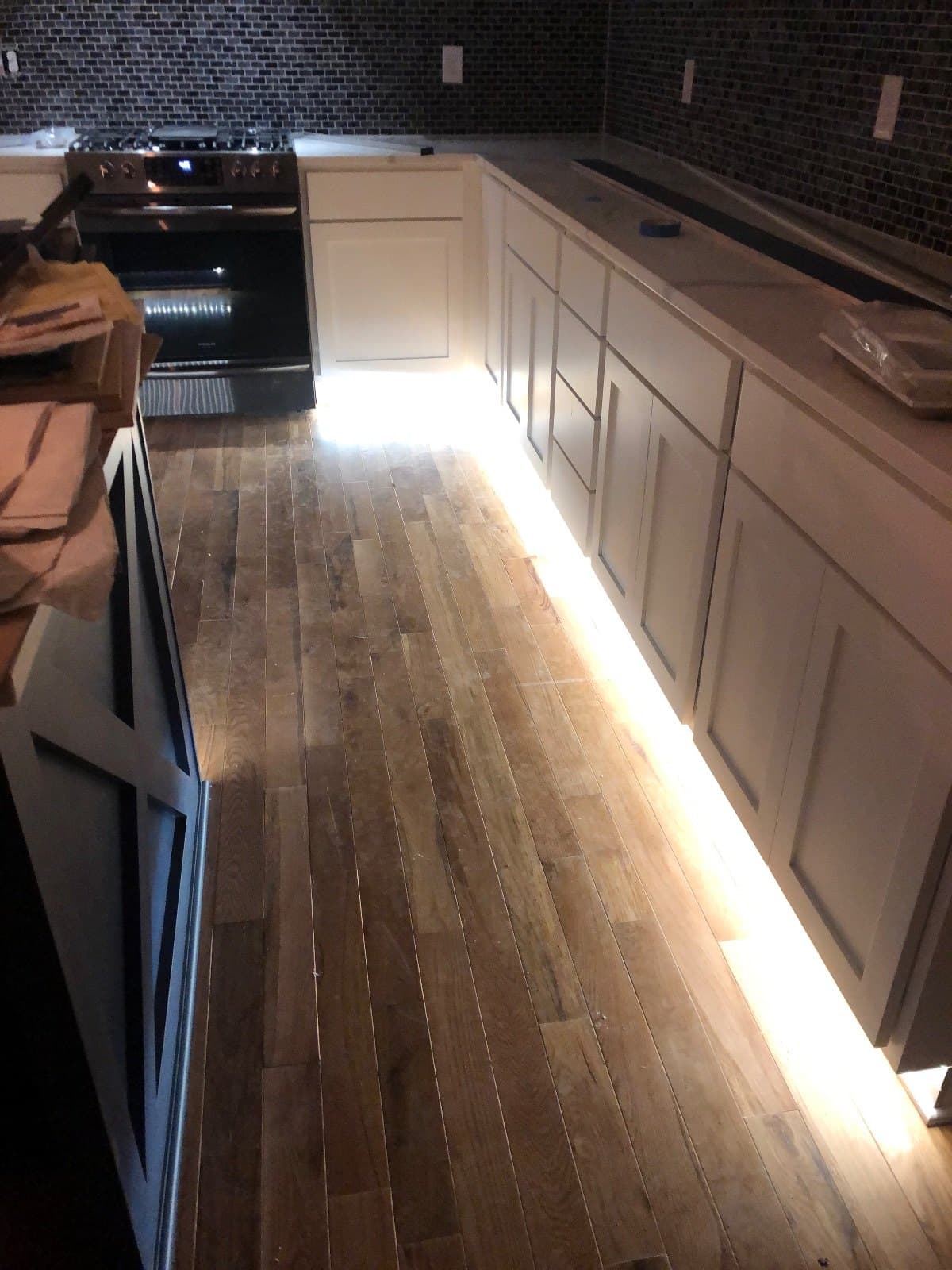 Hardwood laid the length of a kitchen run, packing paper stacked against the wall and work lighting on.