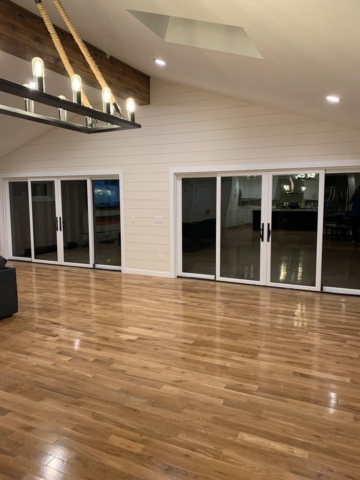 A long great room in hardwood, a beam and a linear light overhead, sliding glass doors across the far wall.