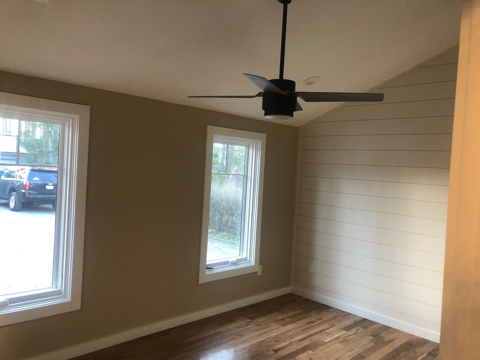 A corner room with two windows and a shiplap wall, hardwood running to the baseboard.