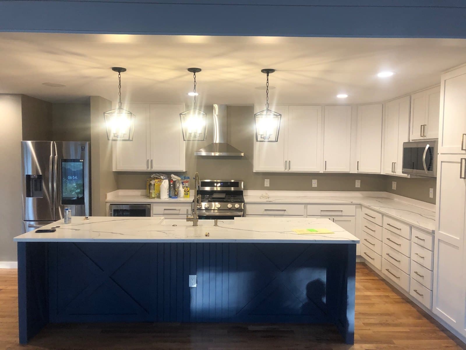 A kitchen with a navy island under three pendant lights, stone counters and a range hood, hardwood beyond.