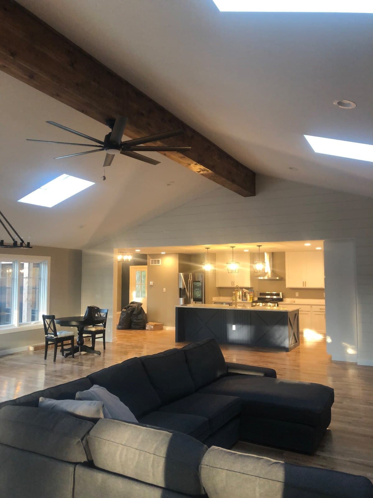 A vaulted great room with a timber beam and glazed roof openings, a sectional in the foreground on hardwood.