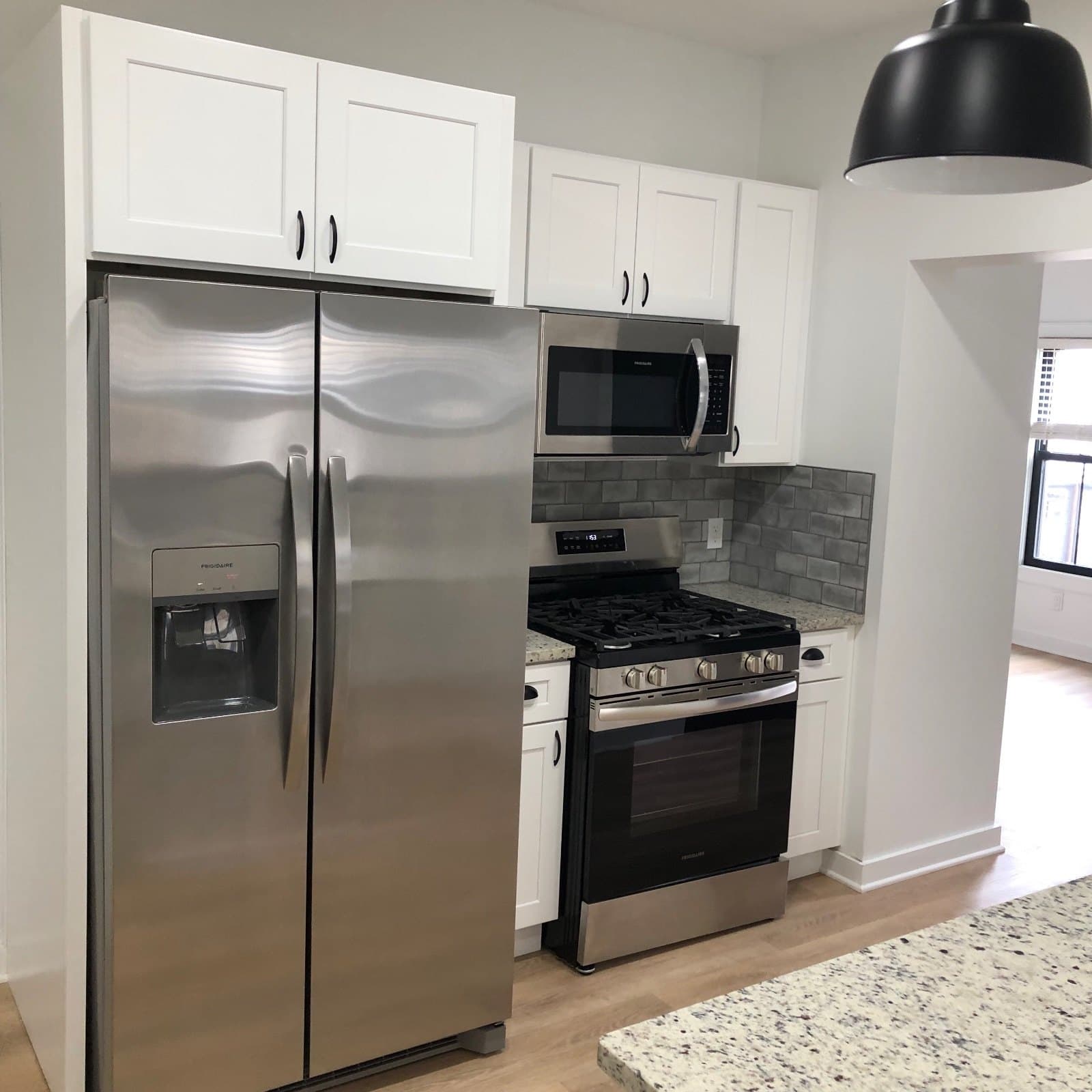 A kitchen with the appliances set and a granite peninsula in the foreground, vinyl plank running out of the room.