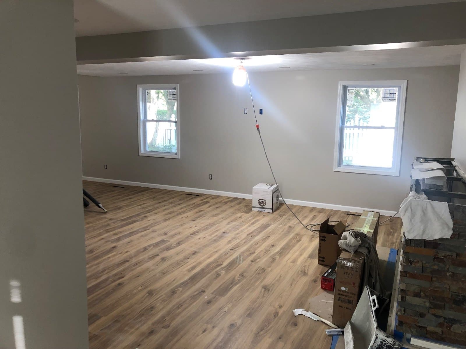 An open room floored in vinyl plank with a bare bulb overhead, cartons and a stone-faced bar part built.